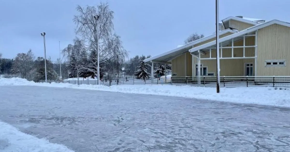 The Mannainen skating field in Kalanti in winter: a cleared ice surface beside a yellow community building, with lamp posts and a snow-covered birch tree. — Männäisten luistelukenttä (Kalanti)
