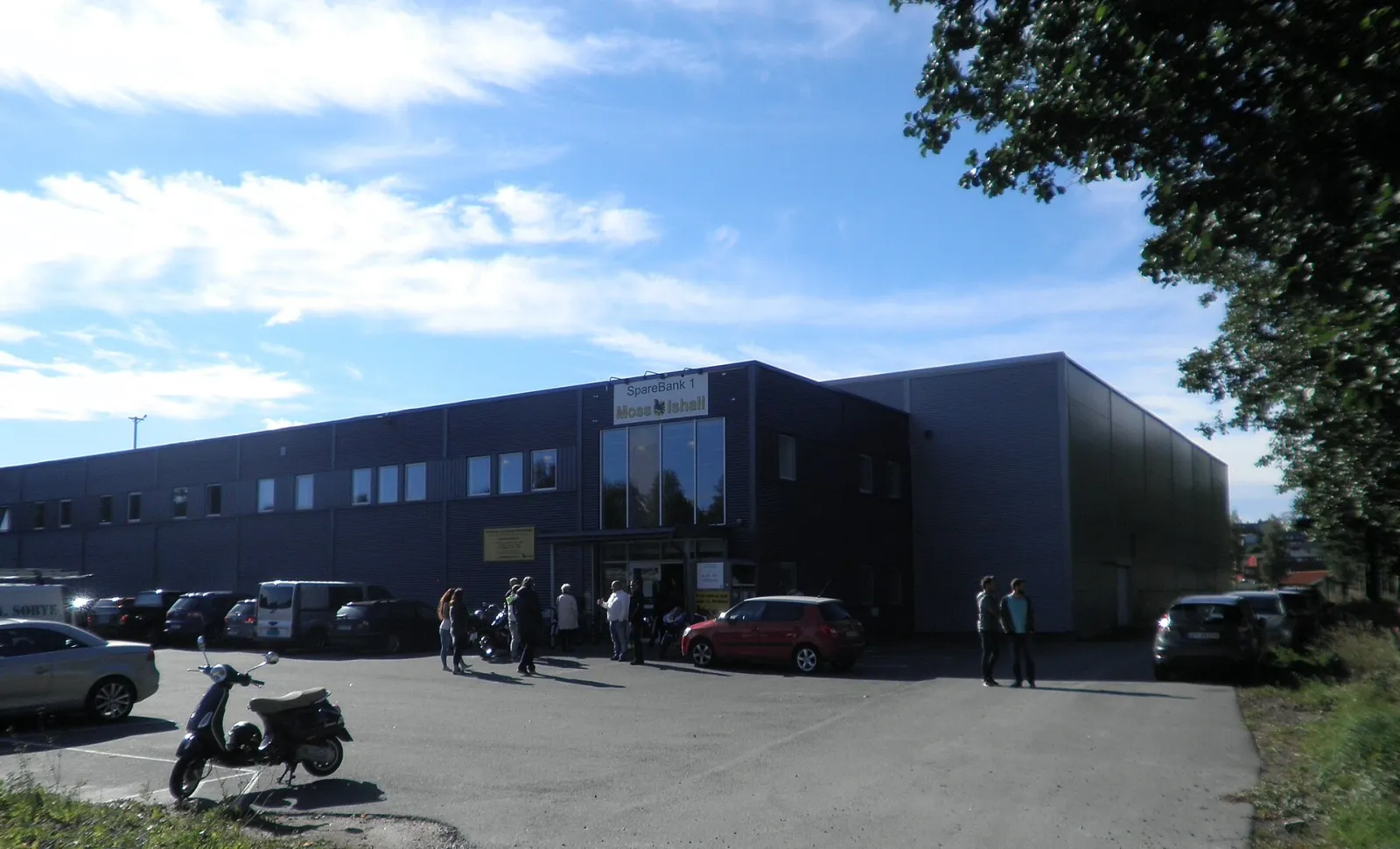 Fronten av Moss ishall, en mørkkledd hall med inngangen og hallens navneskilt over parkeringsplassen. — Marker & Eidsberg Sparebank Ishall