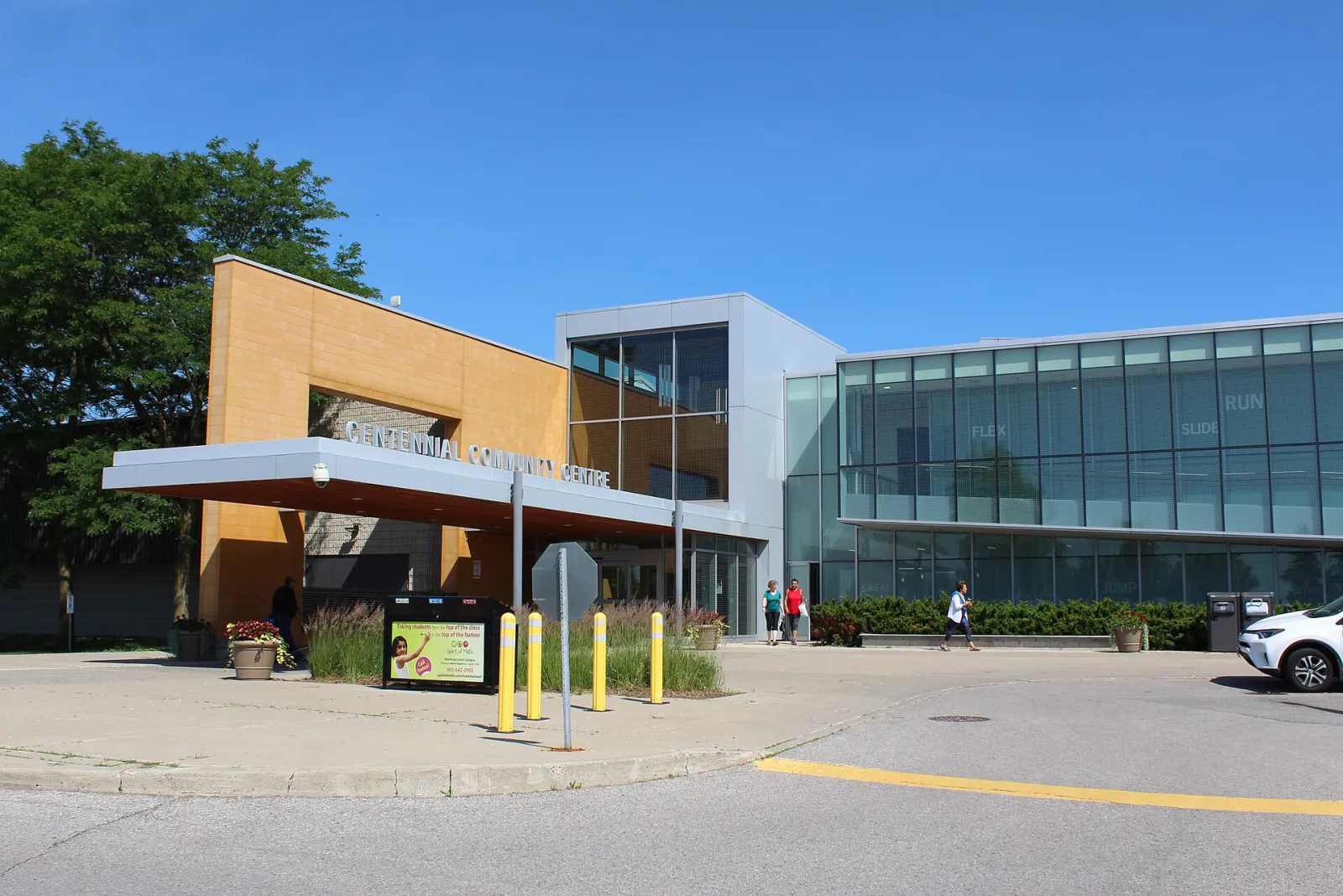 Entrada del Centennial Community Centre: un bloque de ladrillo naranja con una marquesina sobre las puertas y un ala con muros de vidrio a la derecha, con jardineras y bolardos al frente. — Centennial Community Centre (Markham)