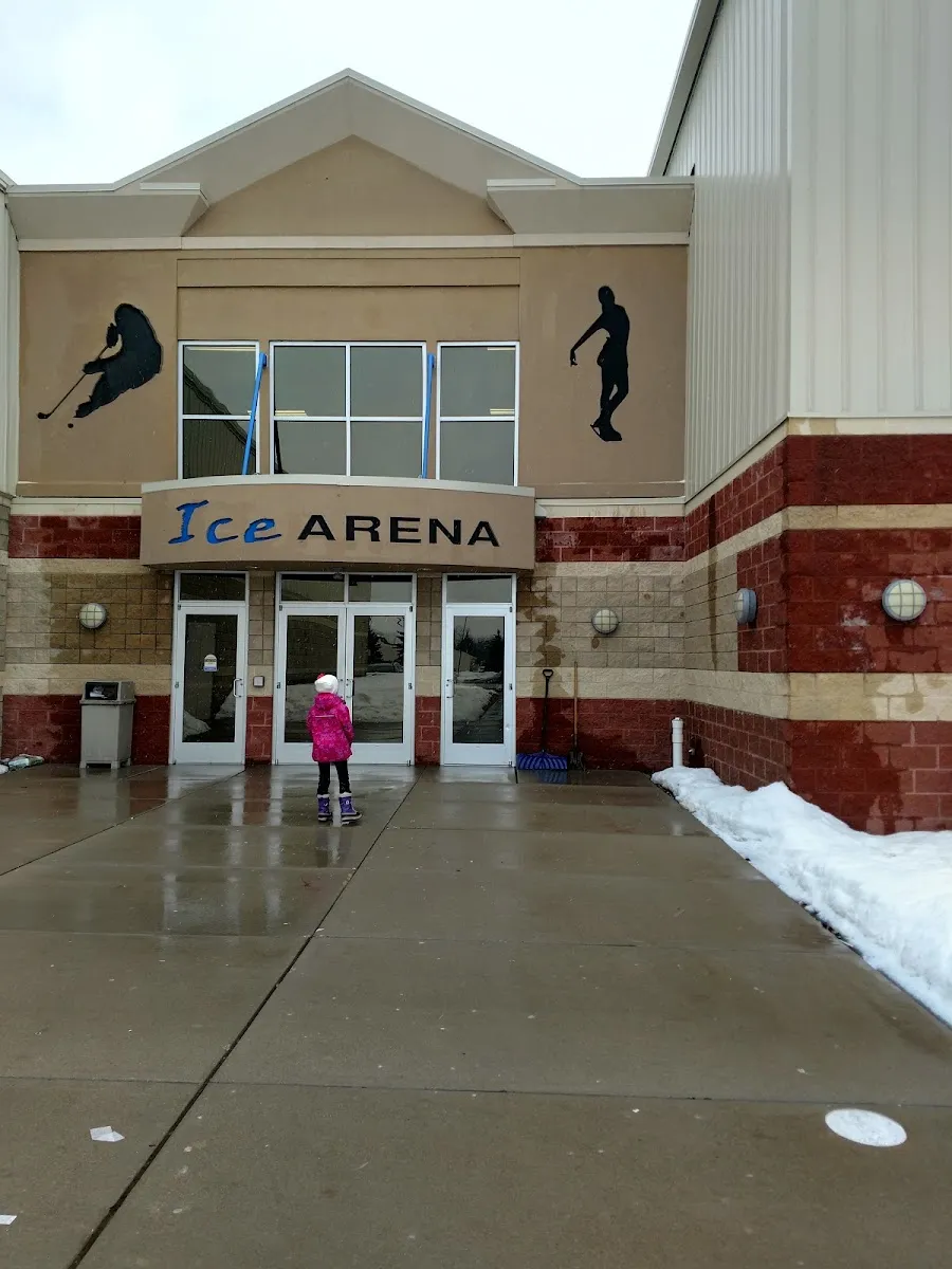 La entrada de la arena bajo un letrero de 'Ice Arena', con siluetas de patinadores en la fachada y muros inferiores de ladrillo. — Martin Ice Arena