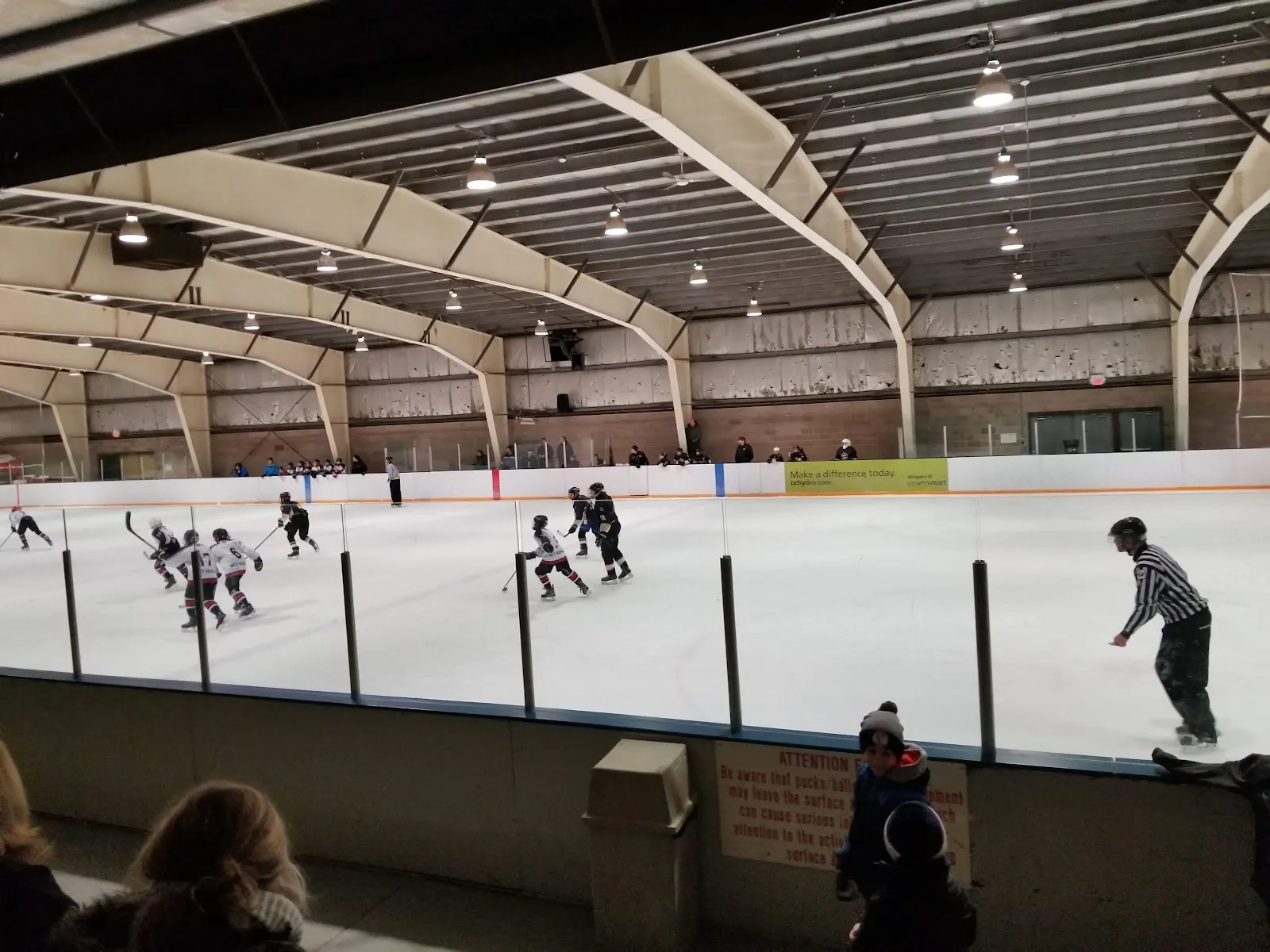 Skaters at a distance on the ice at Marysville Arena, seen across the boards with the roof trusses overhead. — Marysville Arena