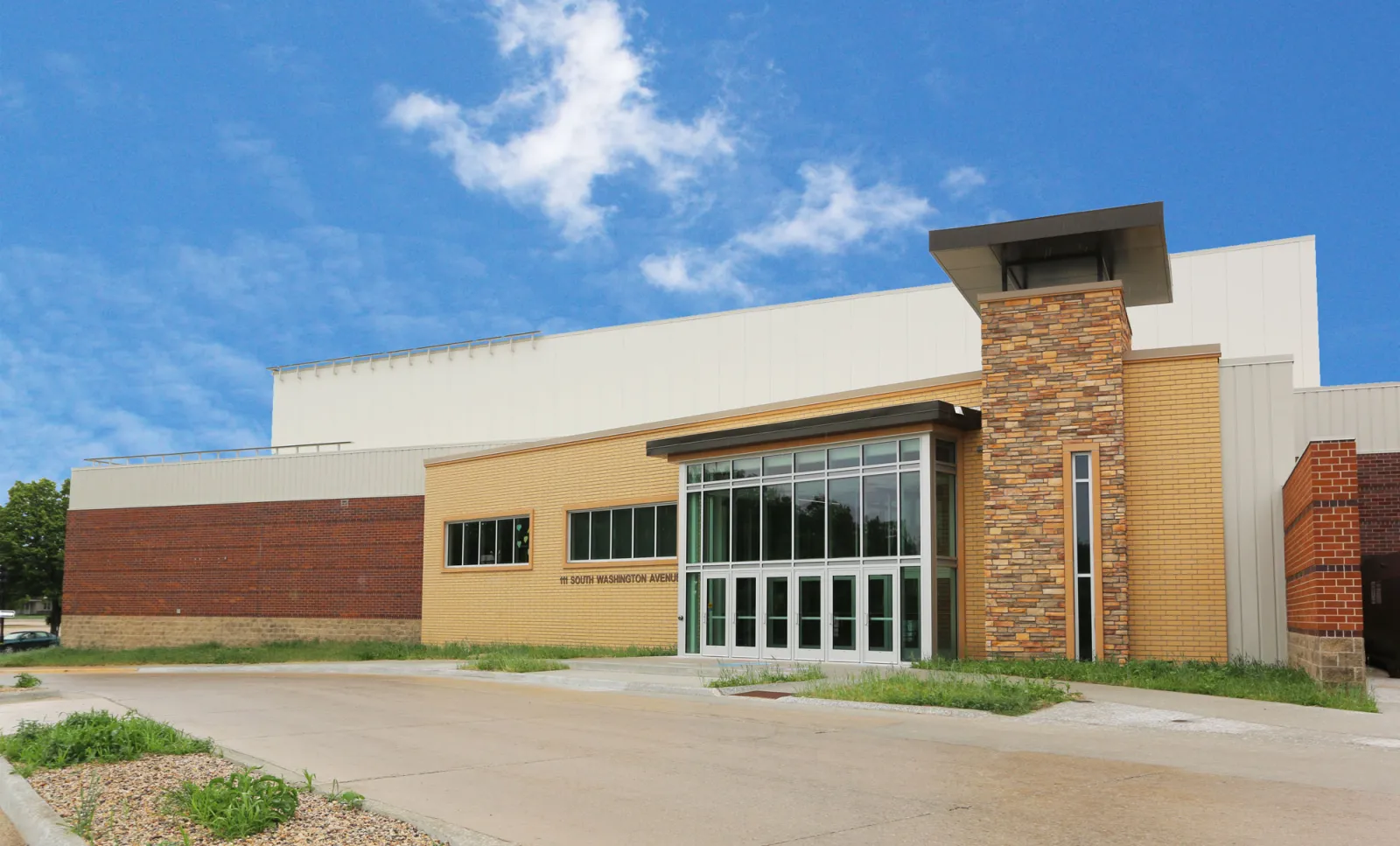The south entrance of Mason City Arena on a sunny day, with a glass entry, stone column and brick walls. — Mason City Arena