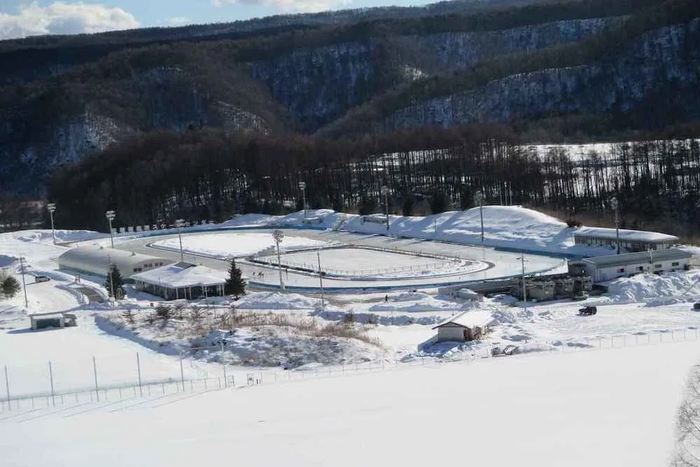 Aerial view of the Matsubarako Kogen Skate Center in winter: the speed-skating oval beside its low buildings, with snow-covered hills behind. — Matsubarako Kogen Skate Center