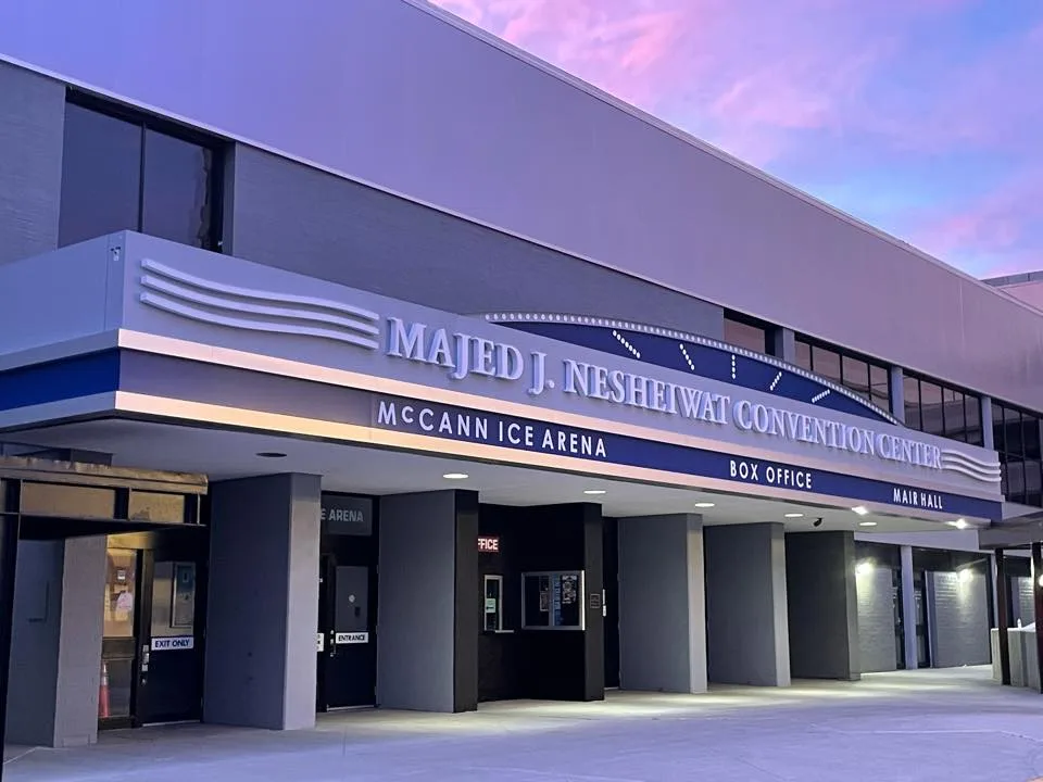 The convention center's entrance canopy at dusk, signed Majed J. Nesheiwat Convention Center with McCann Ice Arena, Box Office and Main Hall lettered beneath. — McCann Ice Arena
