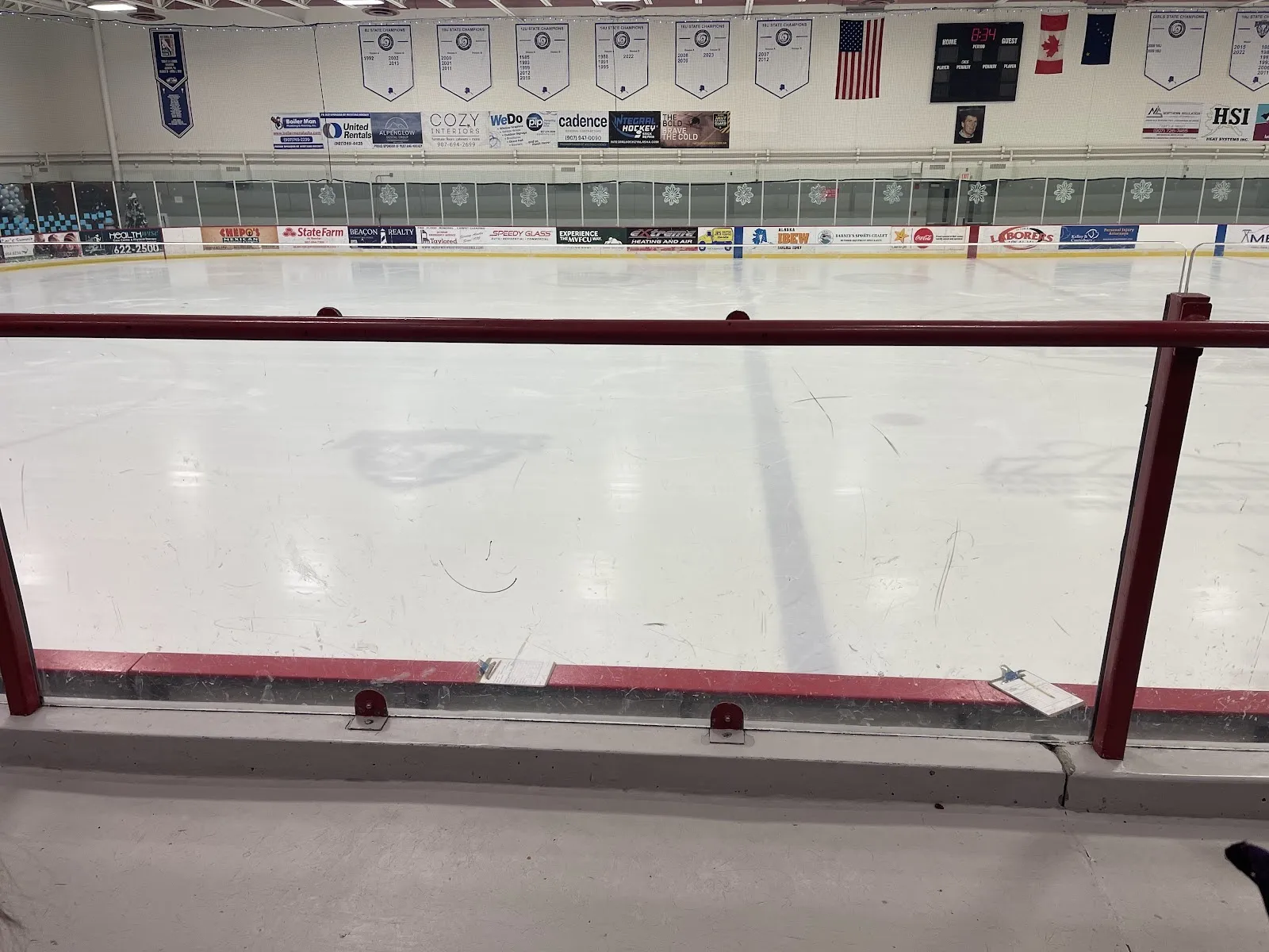 Hielo vacío visto por encima de un barandal rojo, una larga pista con banderines del club y anuncios de patrocinadores en la pared del fondo. — Harry J. McDonald Memorial (MAC)
