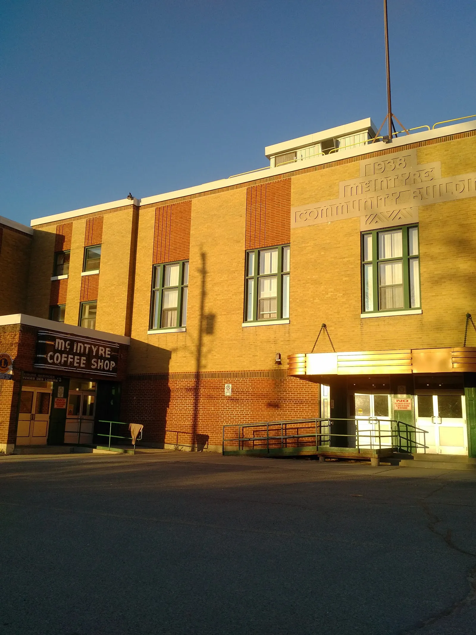 The brick front of the 1938 McIntyre Community Building in Schumacher at dusk, with the McIntyre Coffee Shop entrance sign and the date carved in the stonework. — McIntyre Community Centre (Arena)