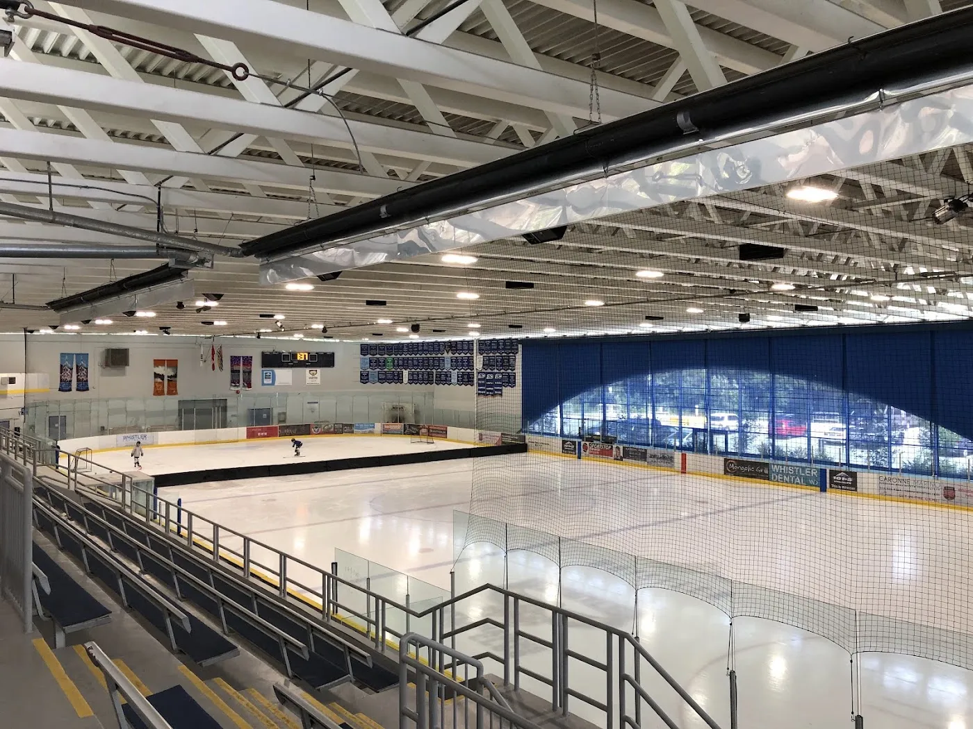 The arena seen from the stands, with the empty ice, blue-and-yellow boards, banners along the far wall and a few skaters at the far end. — Meadow Park Sports Centre
