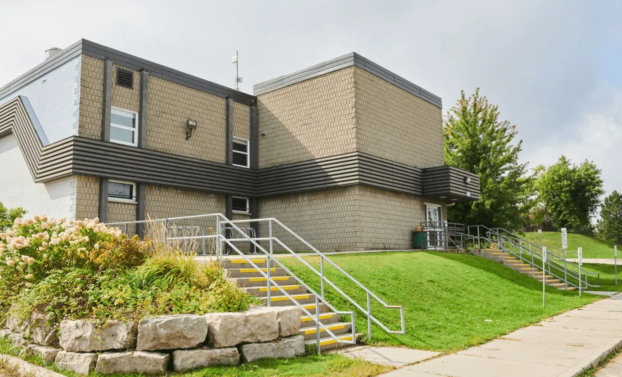 Medway Community Centre, the building that houses Medway Arena: a two-storey tan and dark-banded brick block with a metal railing up a grassy bank to the entrance. — Medway Arena