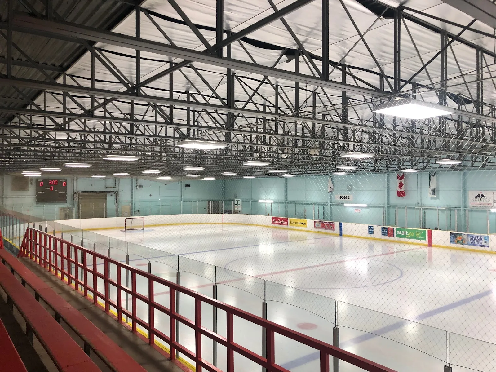The empty rink at Medway seen from the stands, with a red railing in front and steel trusses overhead. — Medway Arena