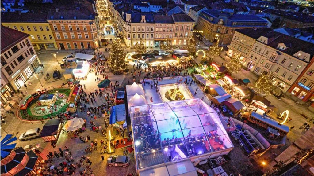Aerial view of the Meiningen on Ice rink on the market square at dusk, with the lit rink tent among the Christmas market stalls and old town buildings. — Meiningen on Ice