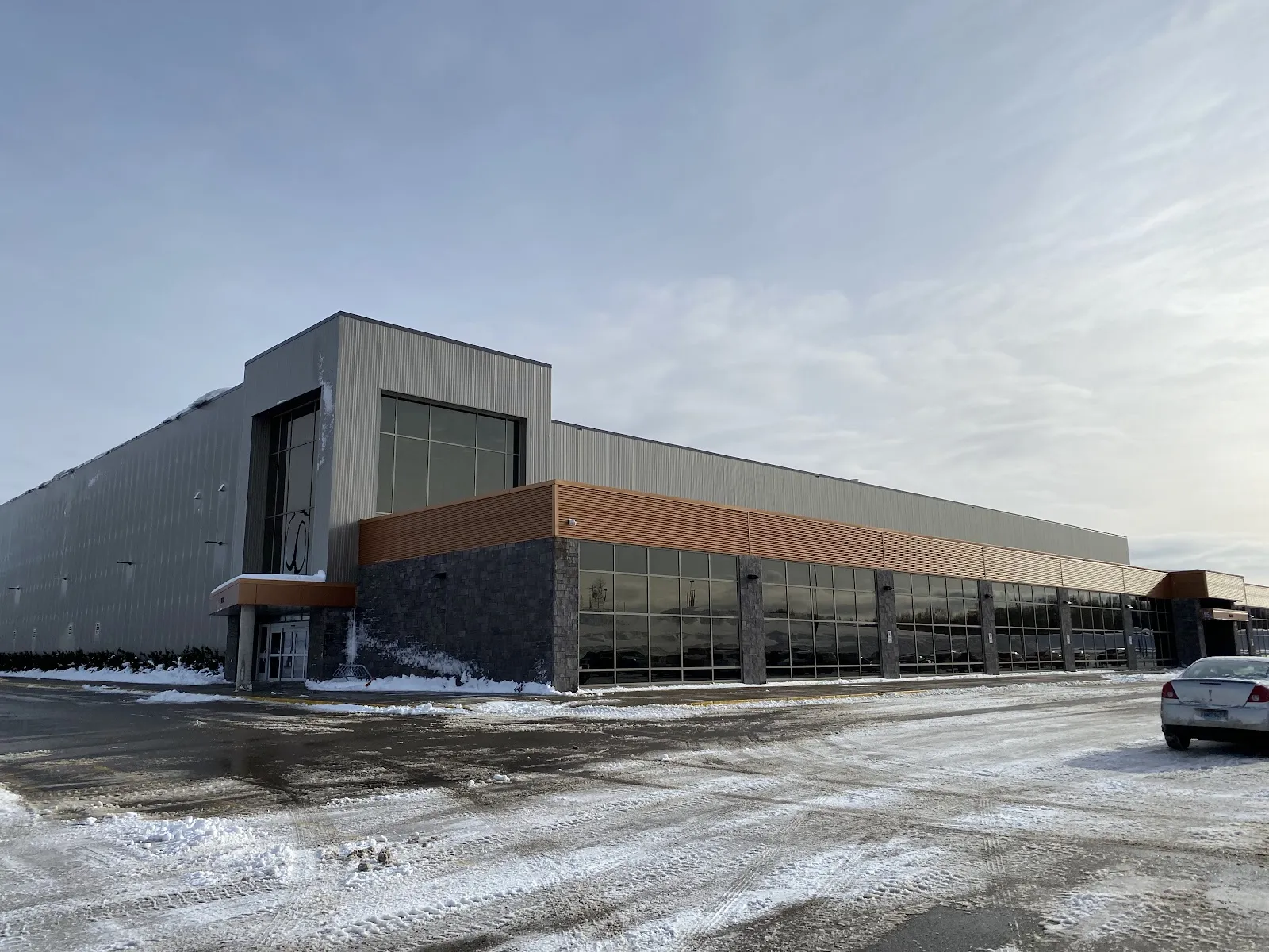The grey metal-clad front of the Membertou Sport & Wellness Centre with its orange-trimmed entrance, seen from the snowy parking lot. — Membertou Sport & Wellness Centre