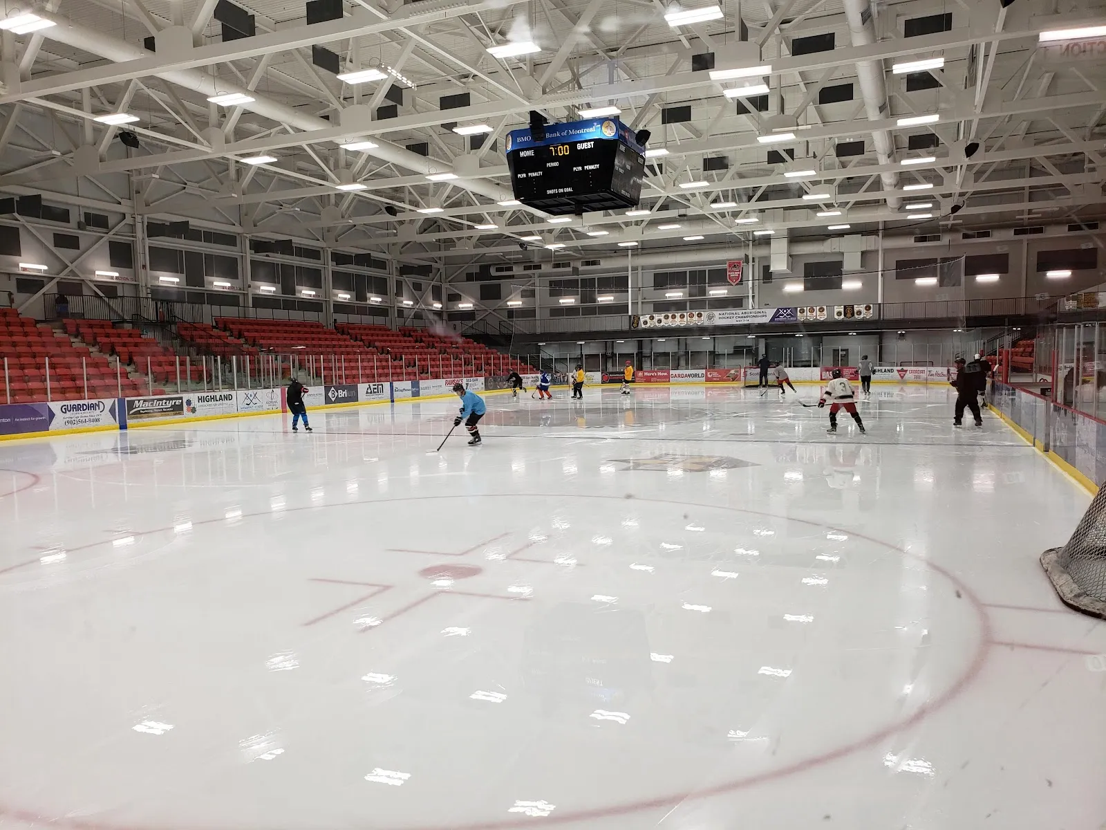 A skating session on the ice at the Membertou Sport & Wellness Centre, with a few skaters on the sheet and the red seating banks rising behind the boards. — Membertou Sport & Wellness Centre