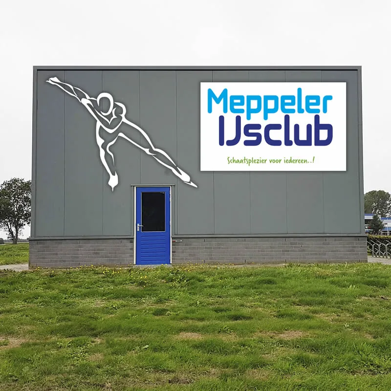 Het grijze clubgebouw van de Meppeler IJsclub met het schaatserslogo en de naam op de wand, op het gras aan de rand van de baan. – Meppeler IJsclub