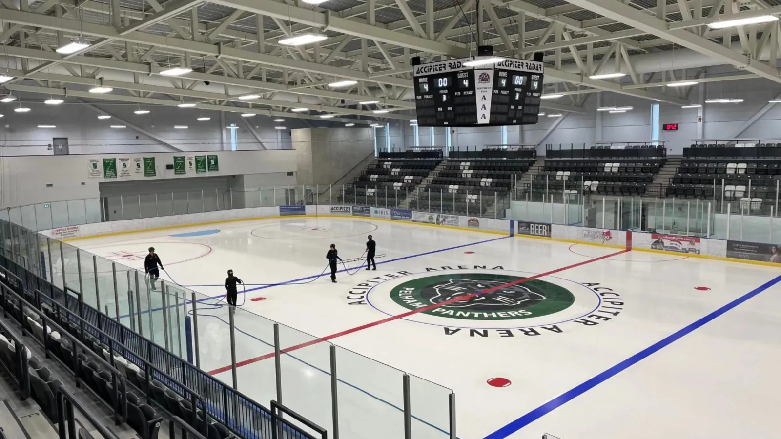 The Accipiter Arena ice with the Panthers logo at centre, a few skaters, raised seating along one side and a scoreboard over the rink. — Meridian Community Centre