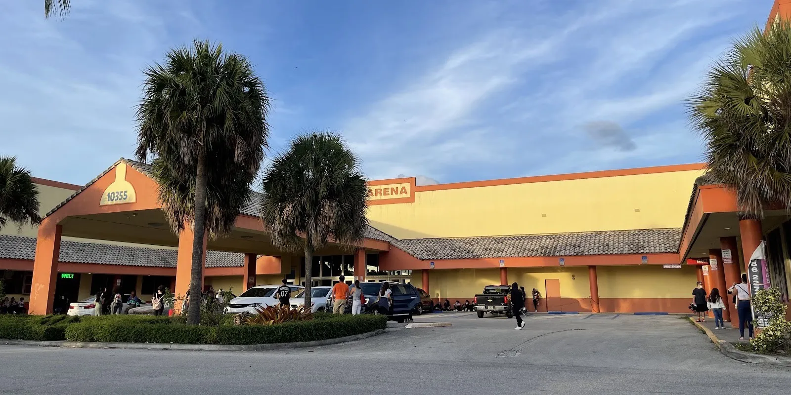 Miami Ice Arena in Kendall: the orange-trimmed porte-cochere at number 10355 under palms, with the tall yellow rink hall and its Arena sign behind — Miami Ice Arena (Kendall)