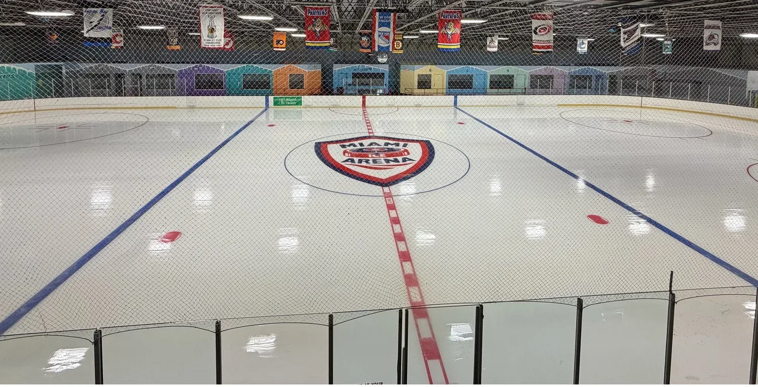 Centre-ice shield and the team boxes, shot through the end netting — Miami Ice Arena (Kendall)