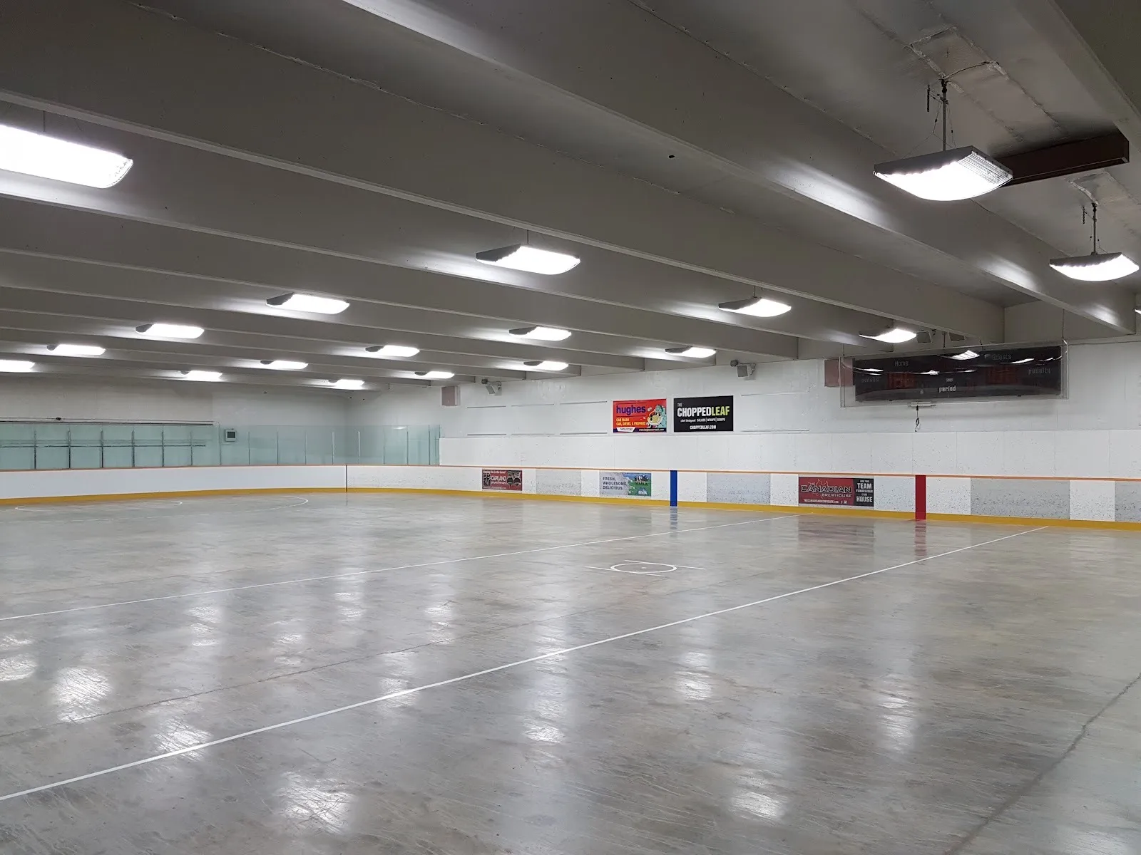 The empty ice at the Michael Cameron Arena in Edmonton, seen from the boards beneath the low ceiling lights — Michael Cameron Arena