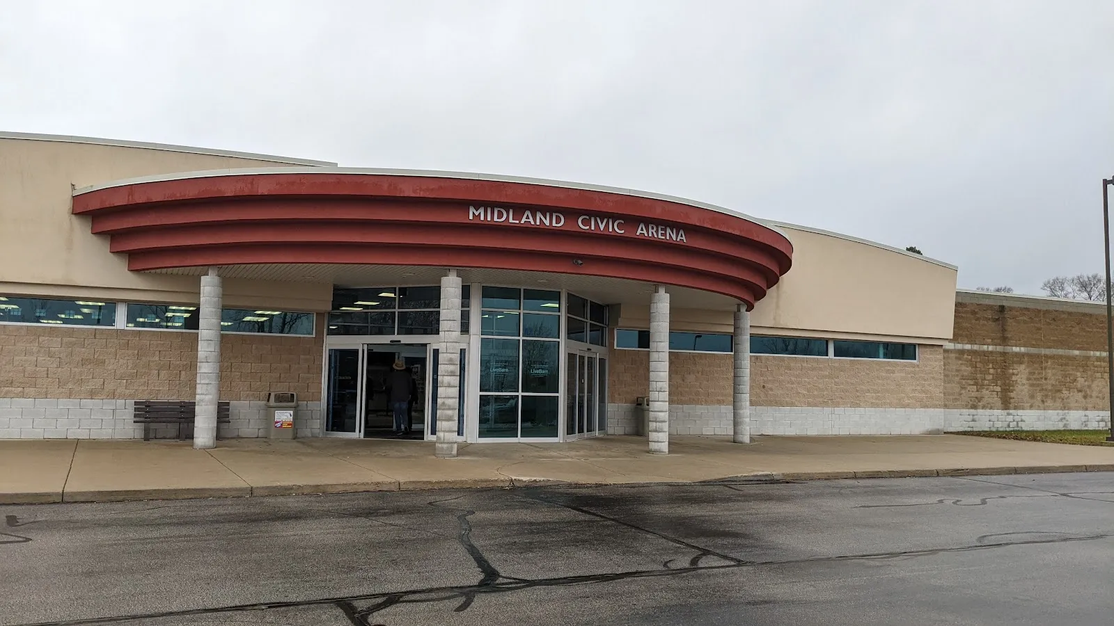 La entrada principal bajo una marquesina roja curva con las letras Midland Civic Arena, con puertas de cristal y muros de ladrillo. — Midland Civic Arena