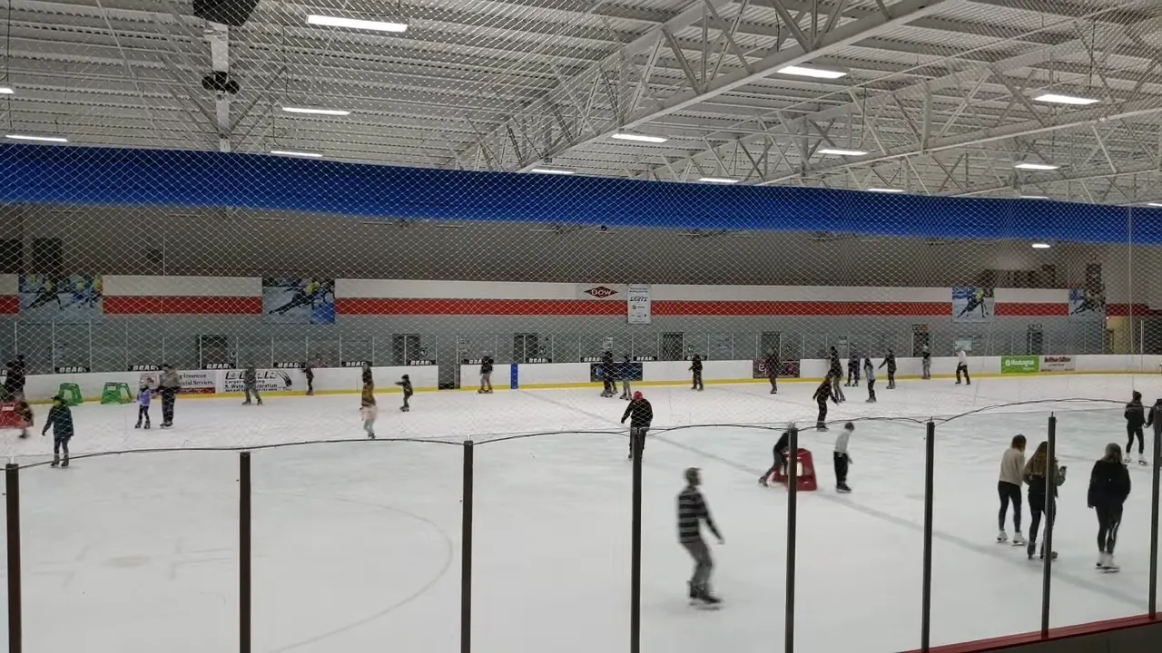 Una sesión de patinaje público en una pista completa detrás del cristal, con un ducto azul en el techo y mantas de patrocinadores a lo largo de la pared del fondo. — Midland Civic Arena