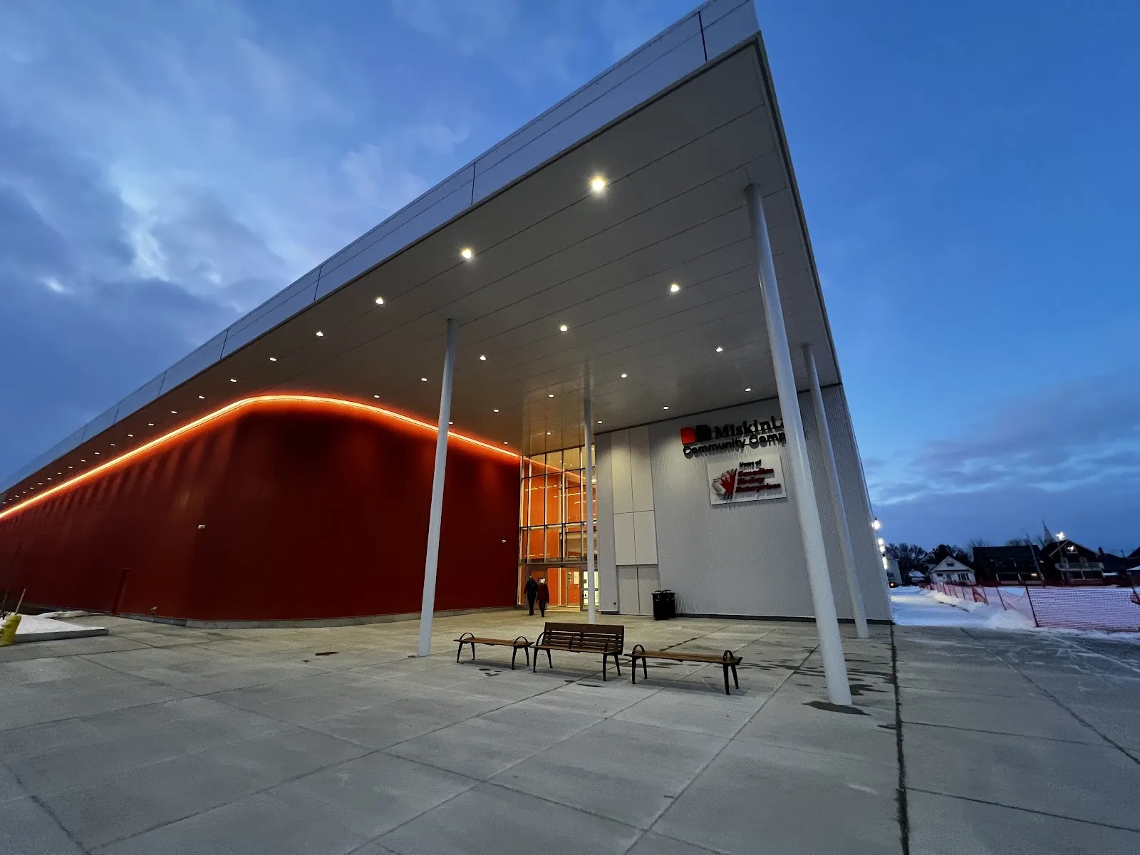 The Miskin Law Community Complex entrance on Lansdowne Street West in Peterborough, with its red wall and long canopy at dusk — Miskin Law Community Complex