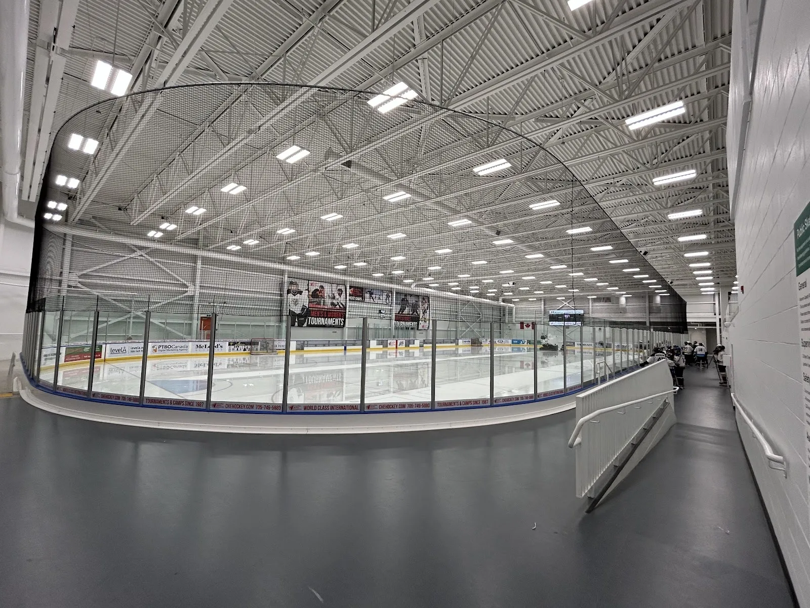 A wide view down the glass of a pale sheet under a long steel-trussed ceiling, a curved boards line and a far wall of white panels. — Miskin Law Community Complex