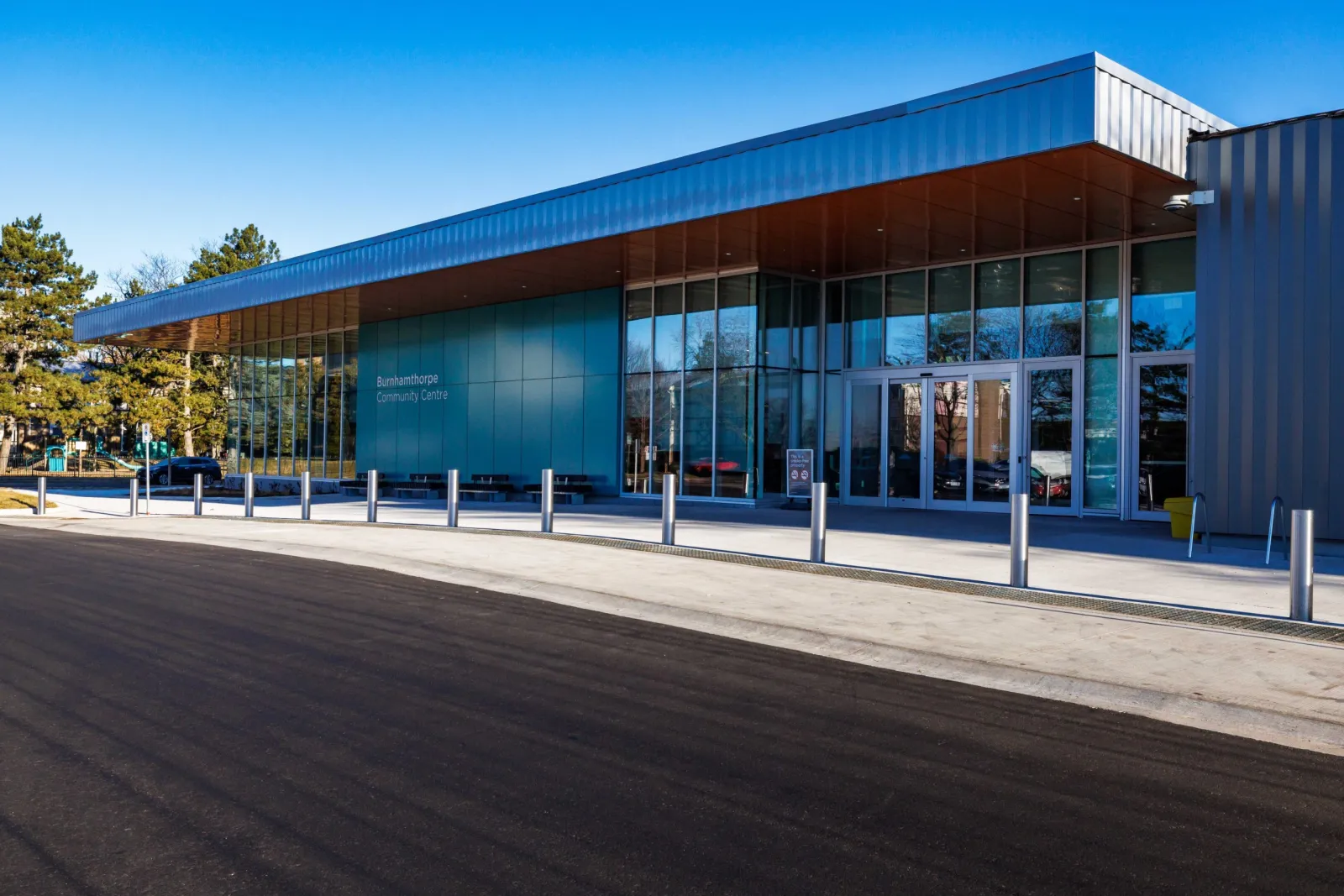 Entrada principal del Burnhamthorpe Community Centre, fachada de vidrio con un letrero iluminado de "Burnhamthorpe Community Centre" en la pared y un alero metálico, de día con cielo despejado — Chic Murray Arena at Burnhamthorpe Community Centre