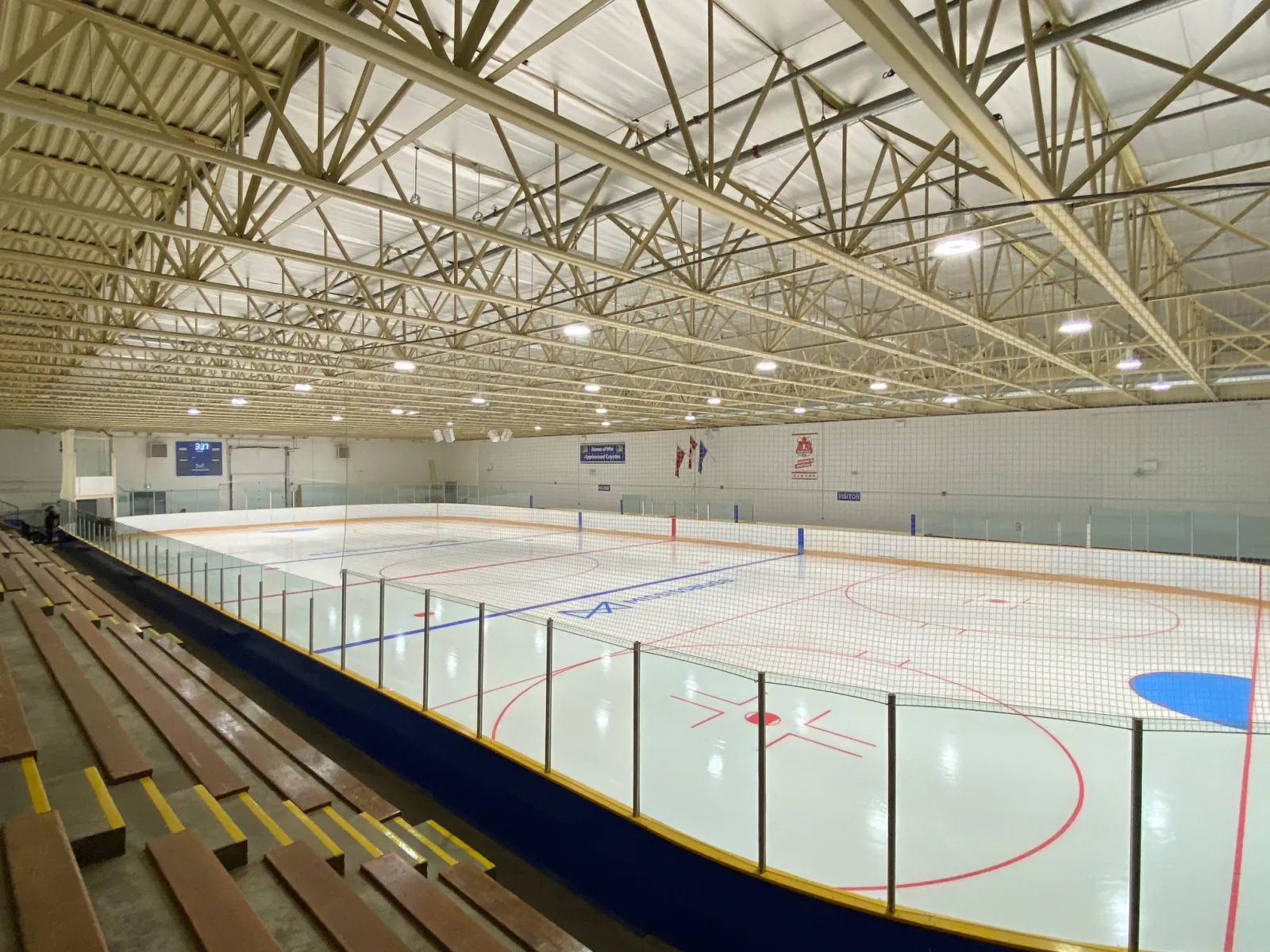 Pista de hielo techada vacía desde las gradas, con todas las marcas de hockey visibles, una manta en la pared que dice "Home of the Applewood Coyotes" y una bandera de Canadá y el escudo de la ciudad de Mississauga en la pared del fondo — Chic Murray Arena at Burnhamthorpe Community Centre
