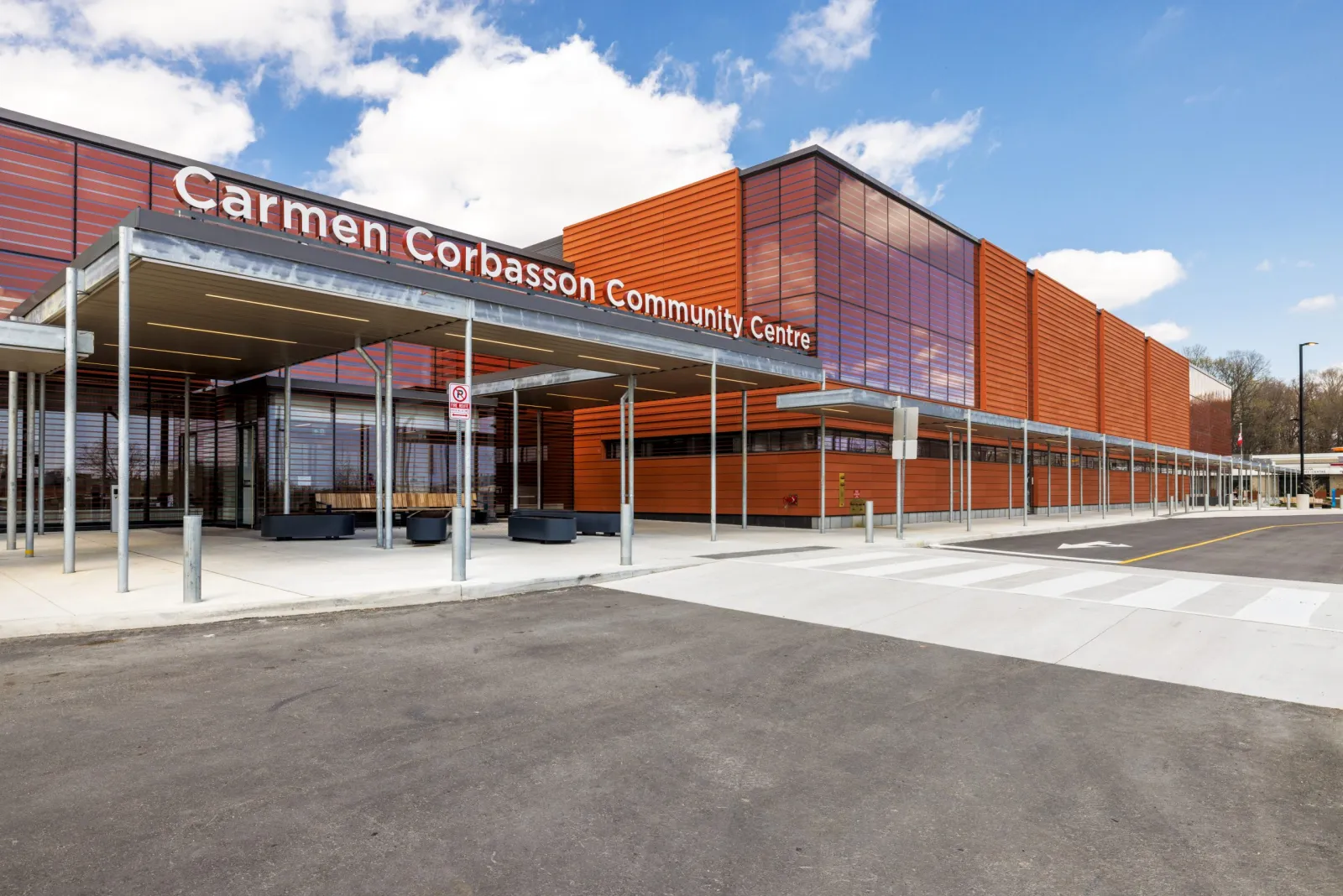 Marquesina de la entrada principal del Carmen Corbasson Community Centre, fachada de paneles metálicos naranjas con grandes letras de "Carmen Corbasson Community Centre" en la pared, de día con cielo azul — Carmen Corbasson Community Centre Arenas