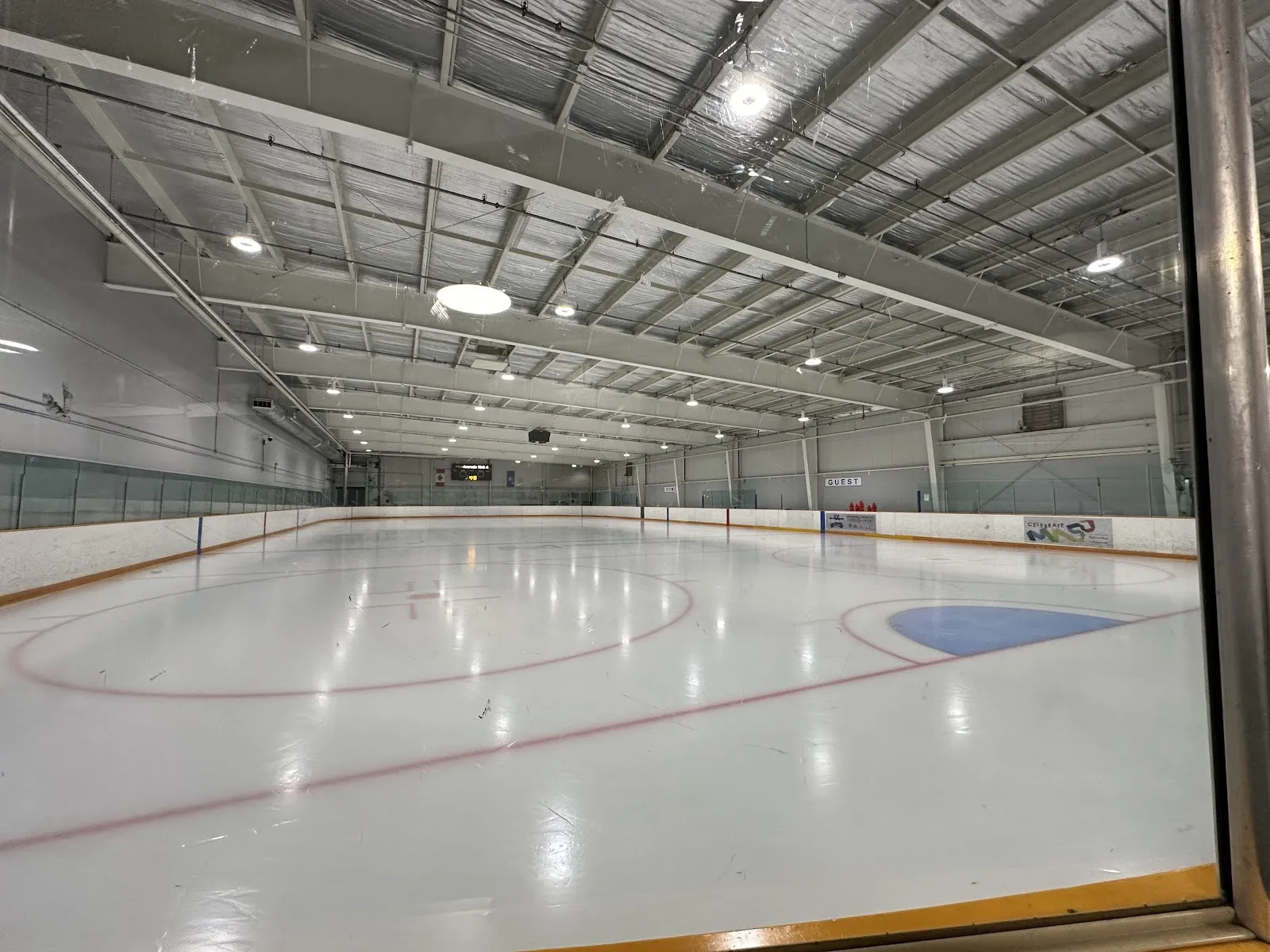 Pista de hielo vacía en Meadowvale 4 Rinks, vista por encima de las vallas hacia el extremo opuesto, con un letrero de identificación de la pista y anuncios en las vallas visibles. — Meadowvale 4 Rinks