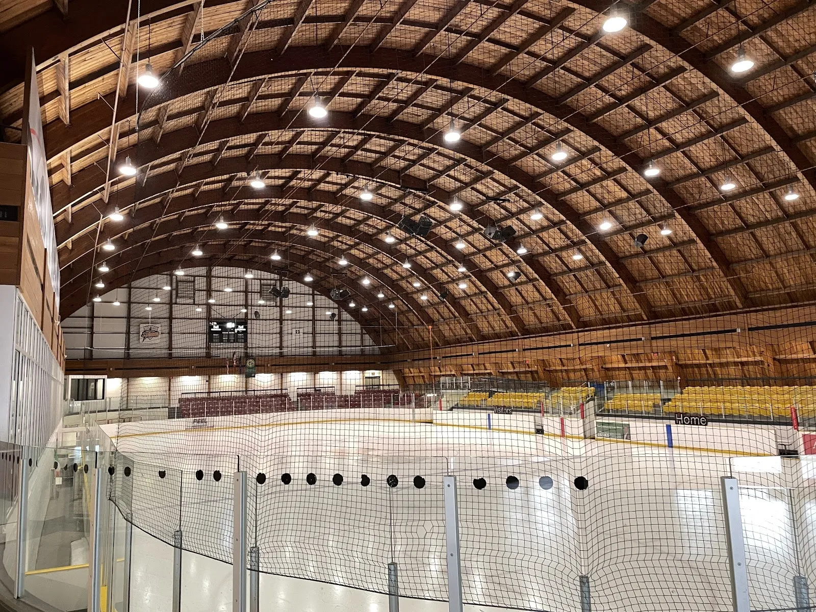 La arena de Port Credit con techo arqueado vista desde el vidrio de la pista, con la pista vacía bajo una amplia bóveda de cañón de madera con una franja de ventanas en el extremo. — Port Credit Memorial Arena