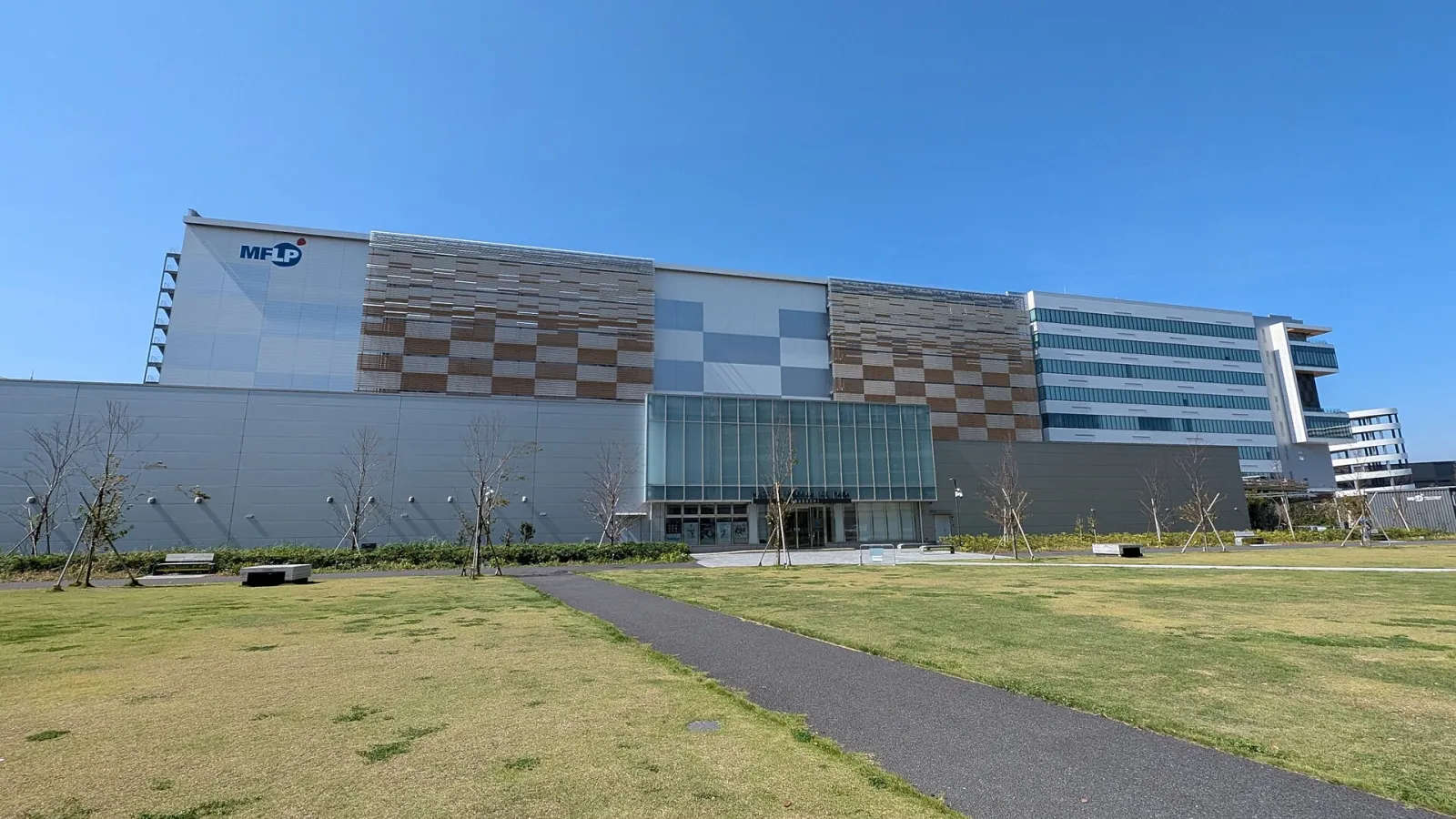 芝生越しに見た、船橋のMFLP船橋の建物。中央のガラスの入口棟が、三井不動産アイスパーク船橋につながっています — Mitsui Fudosan Ice Park Funabashi