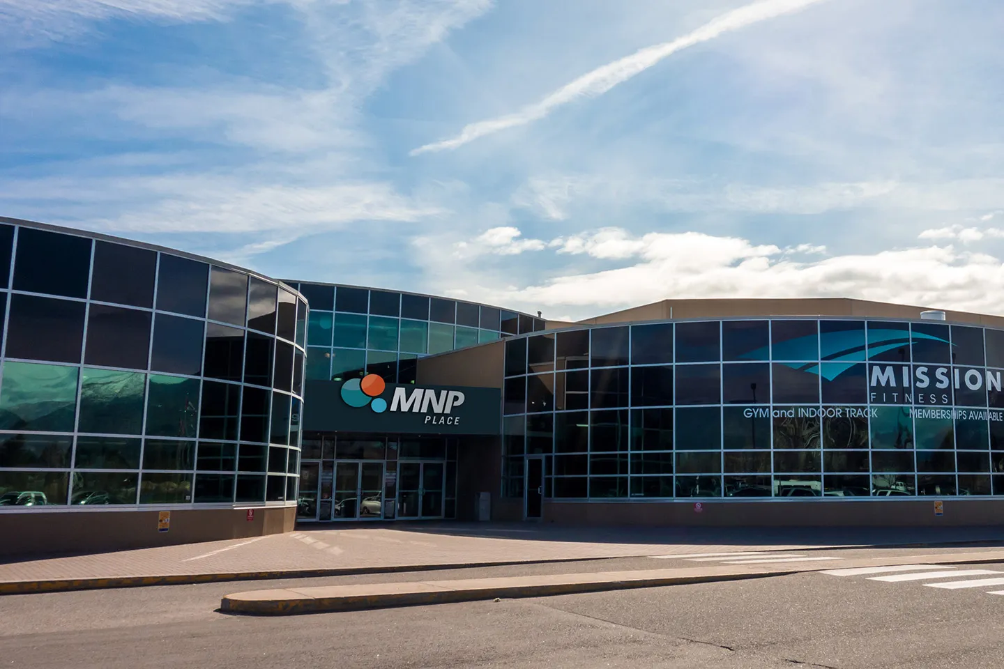 MNP Place's glass-fronted entrance under a blue sky, with the MNP Place sign above the doors and the Mission Fitness gym signage on the adjoining wing — MNP Place