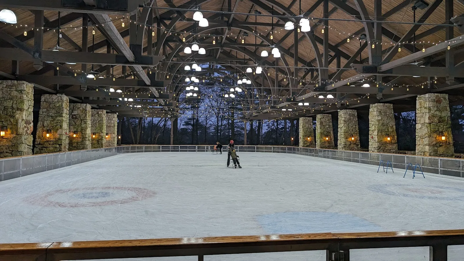 A lone skater on the ice inside the timber-framed Mohonk skating pavilion, with the open roof trusses above the boards. — Mohonk Mountain House Ice Skating Pavilion