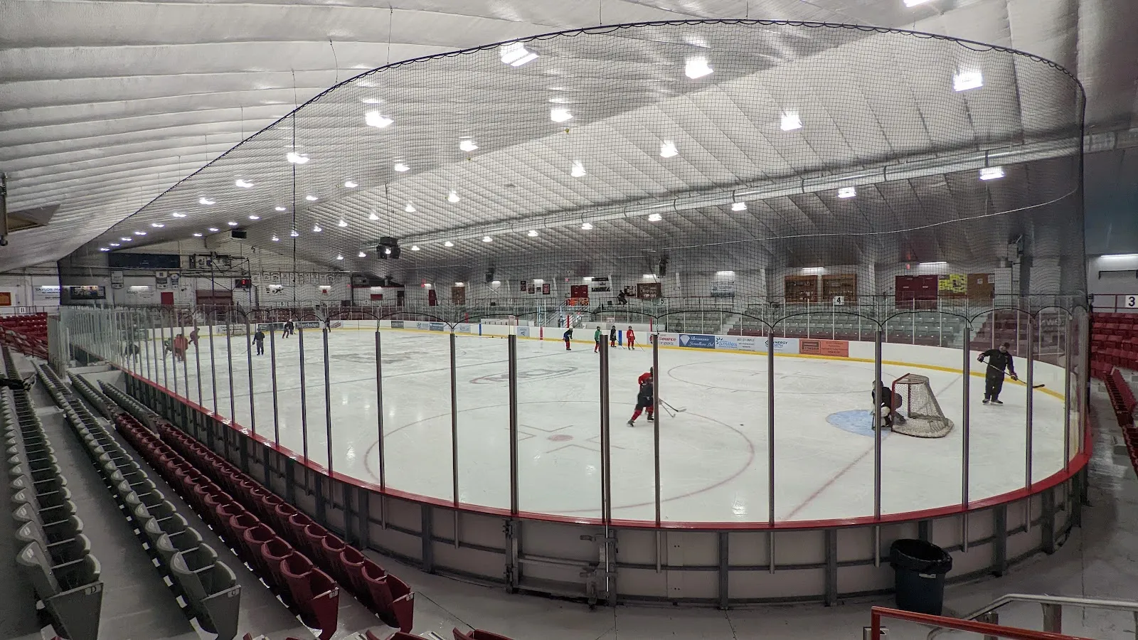 The Thistle rink from the red seats, with a practice at the far end under the curved white roof. — Moncrief Construction Sports Centre (Kenora)