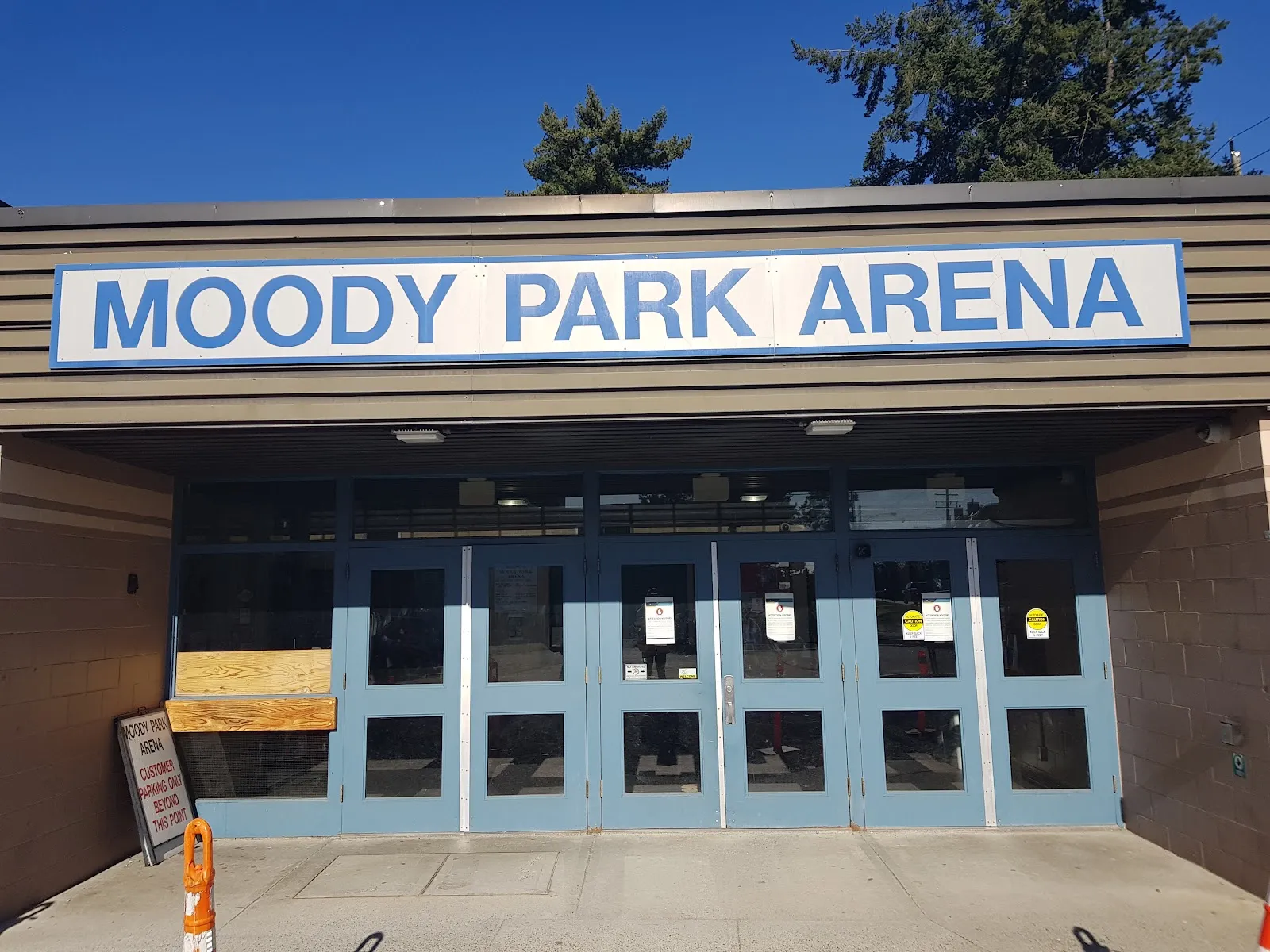 The blue double doors of Moody Park Arena under its large Moody Park Arena sign, seen from the front walkway on a sunny day. — Moody Park Arena