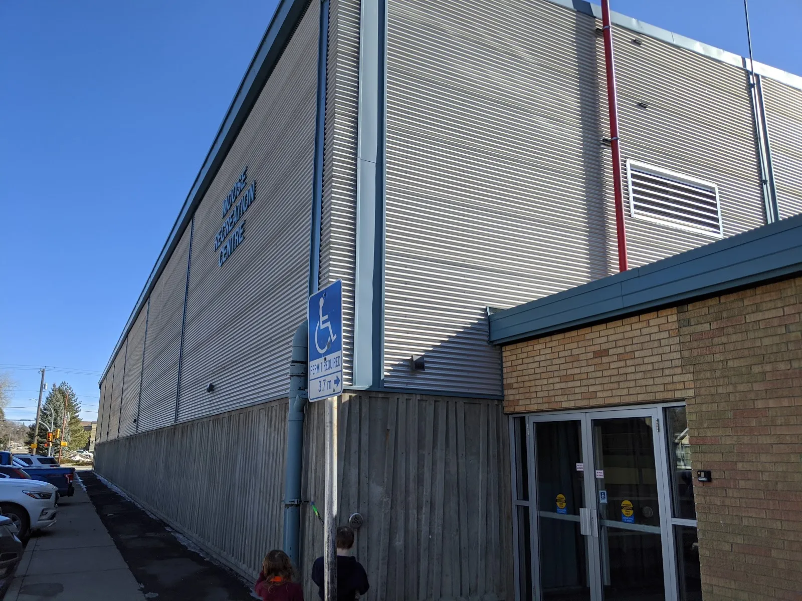The Moose Recreation Centre's tall grey metal-clad wall with its name, beside a brick entrance and an accessible parking sign. — Moose Recreation Centre