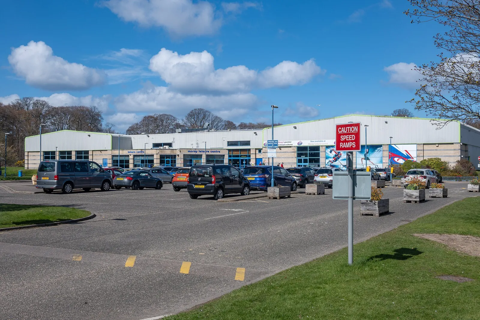 The low, long front of Moray Leisure Centre across its car park on a sunny day. — Moray Leisure Centre