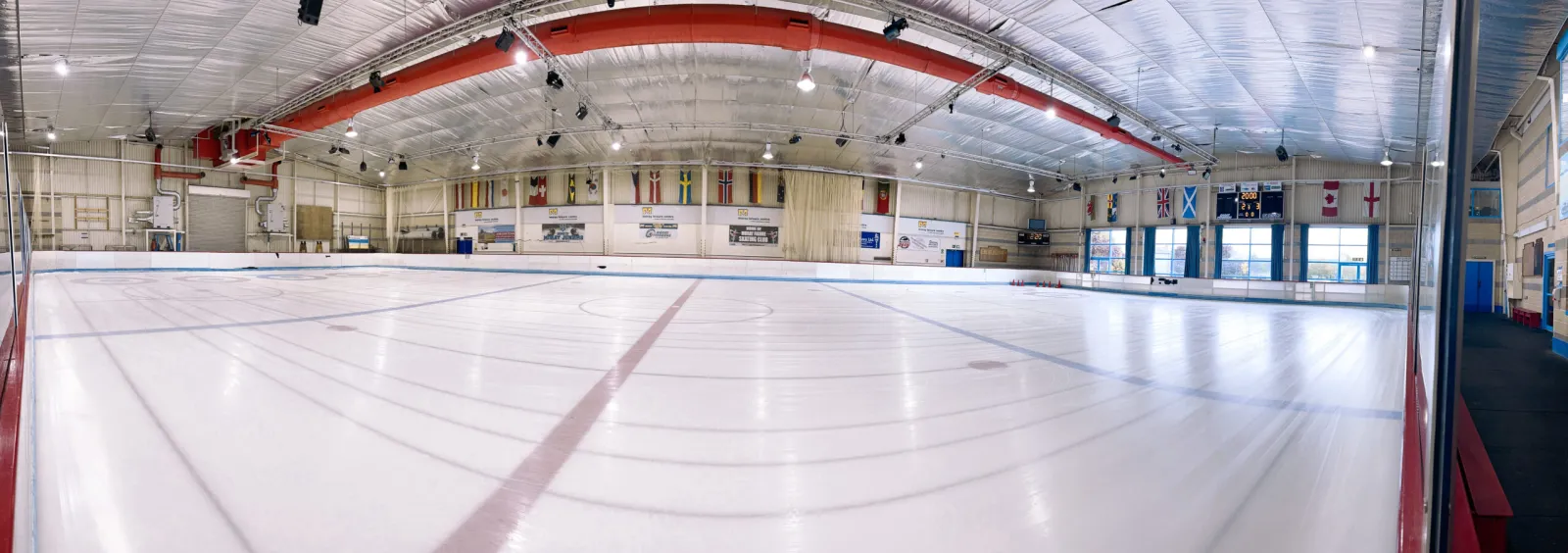 The empty ice from one end, with the curved red roof beam, banners and boards along the far side. — Moray Leisure Centre