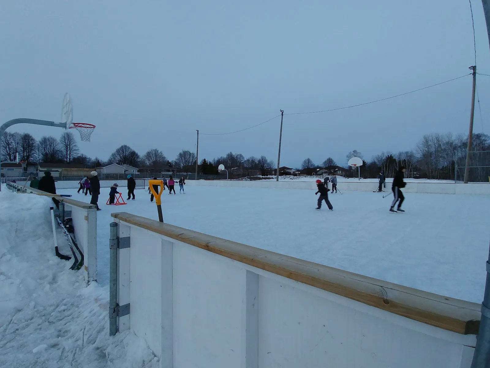 Skaters in the distance on the boarded rink, seen along the boards on a winter day. — Morel Family Foundation Park Outdoor Rink