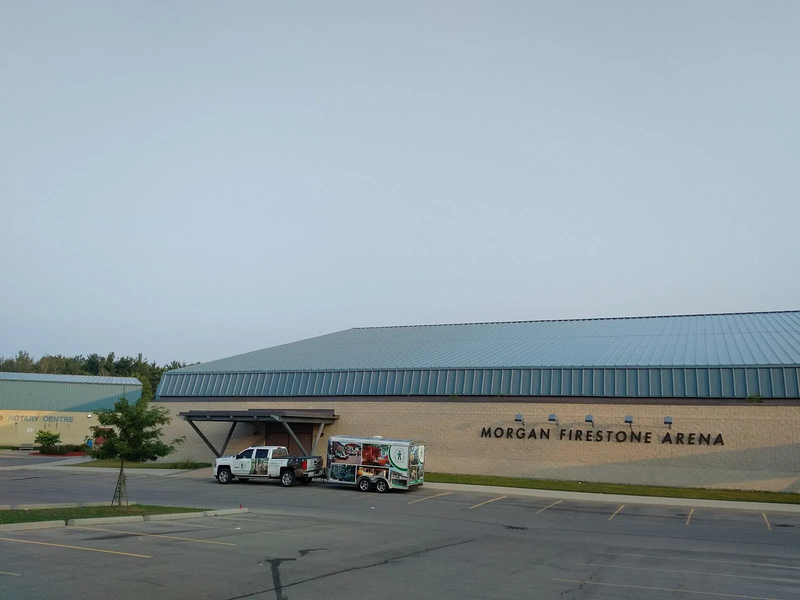 Long low arena building with a blue metal roof and "Morgan Firestone Arena" lettering along the wall, parking lot in front. — Morgan Firestone Arena