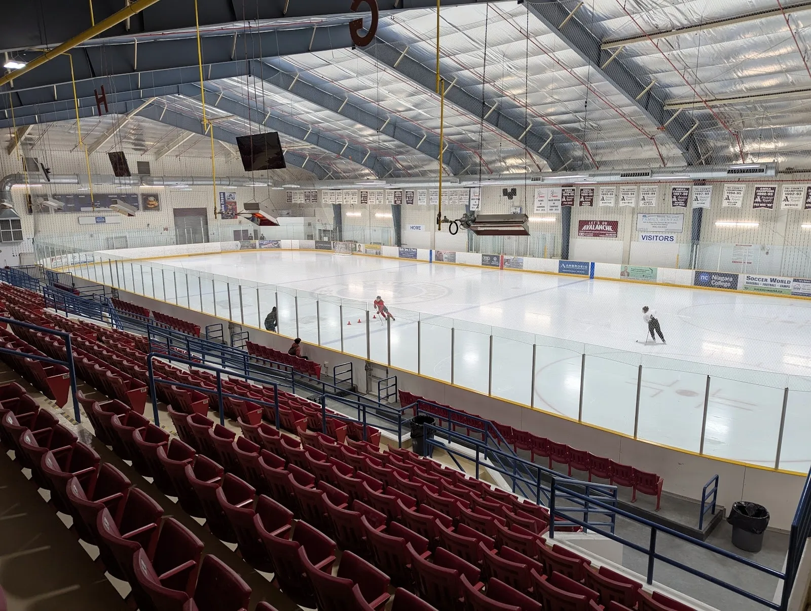 A wide view of the sheet from the upper seats, red-seated grandstands along the near side and a long steel-trussed roof overhead. — Morgan Firestone Arena