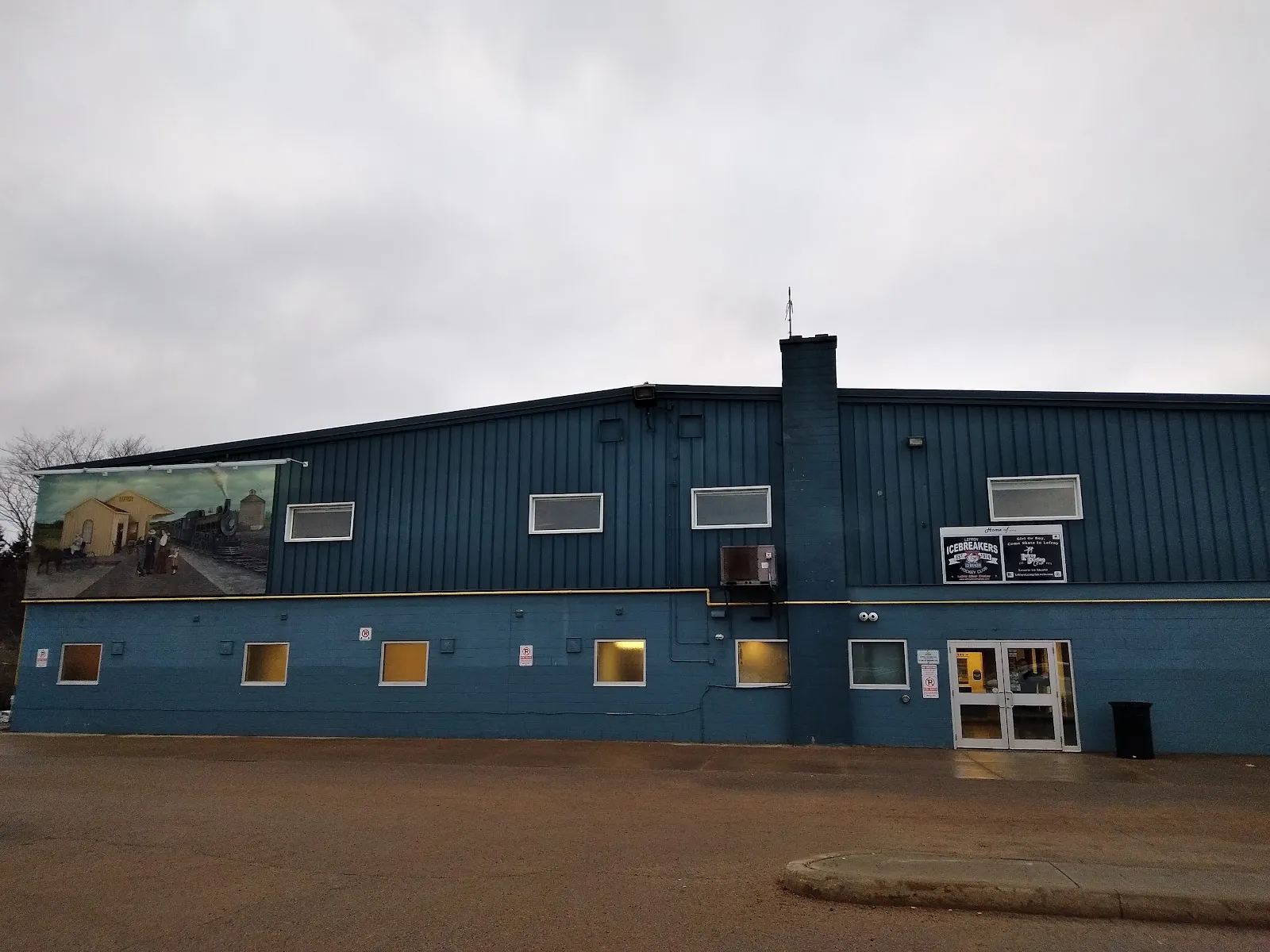 The dark-blue metal-clad side of Morgan Russell Memorial Arena in Lefroy, with a painted mural at the left end and the entrance doors — Morgan Russell Memorial Arena (Lefroy)