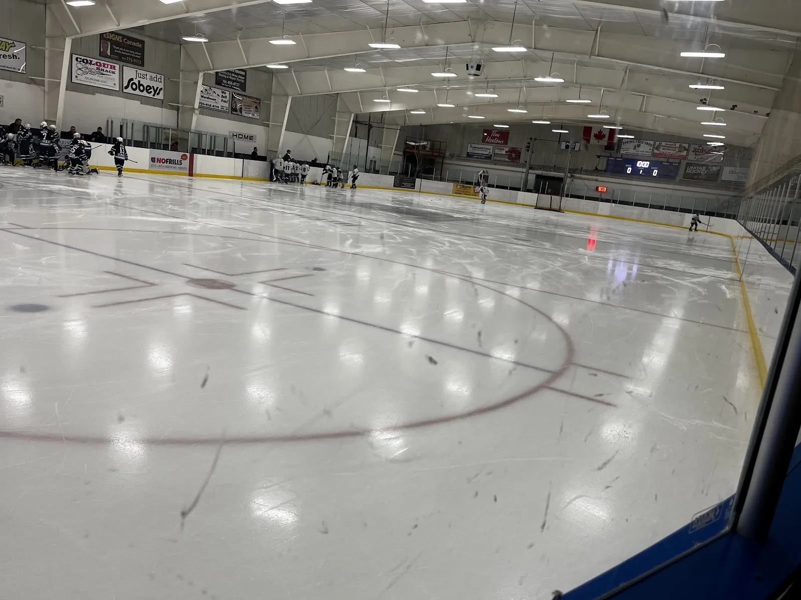 An empty bright sheet seen over the boards from a corner, white ice with a faint circle and blue-lined boards under a white arched ceiling. — Morgan Russell Memorial Arena (Lefroy)