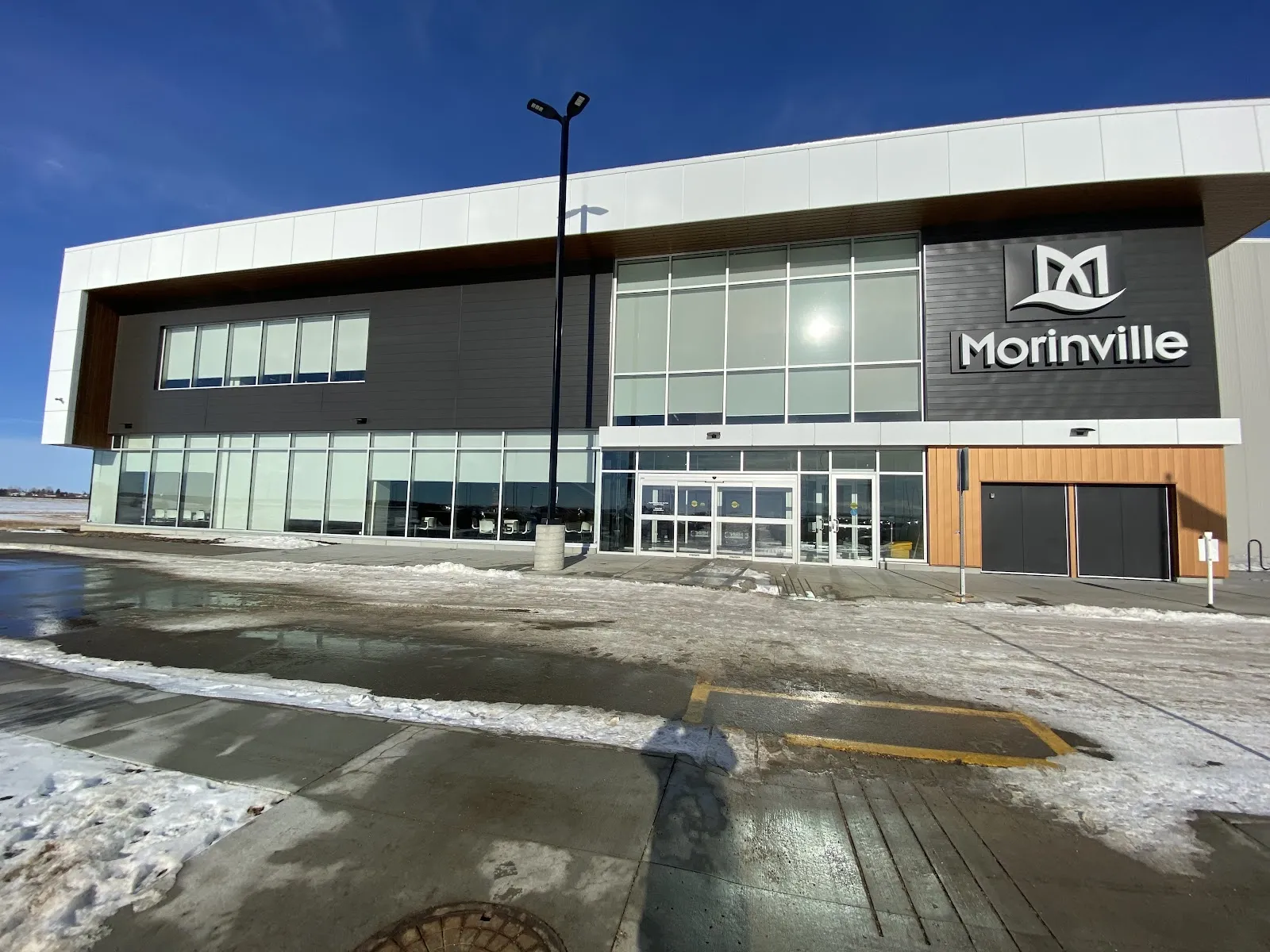The Morinville Leisure Centre front with its glazed entrance and a corner sign on a snowy day. — Morinville Leisure Centre