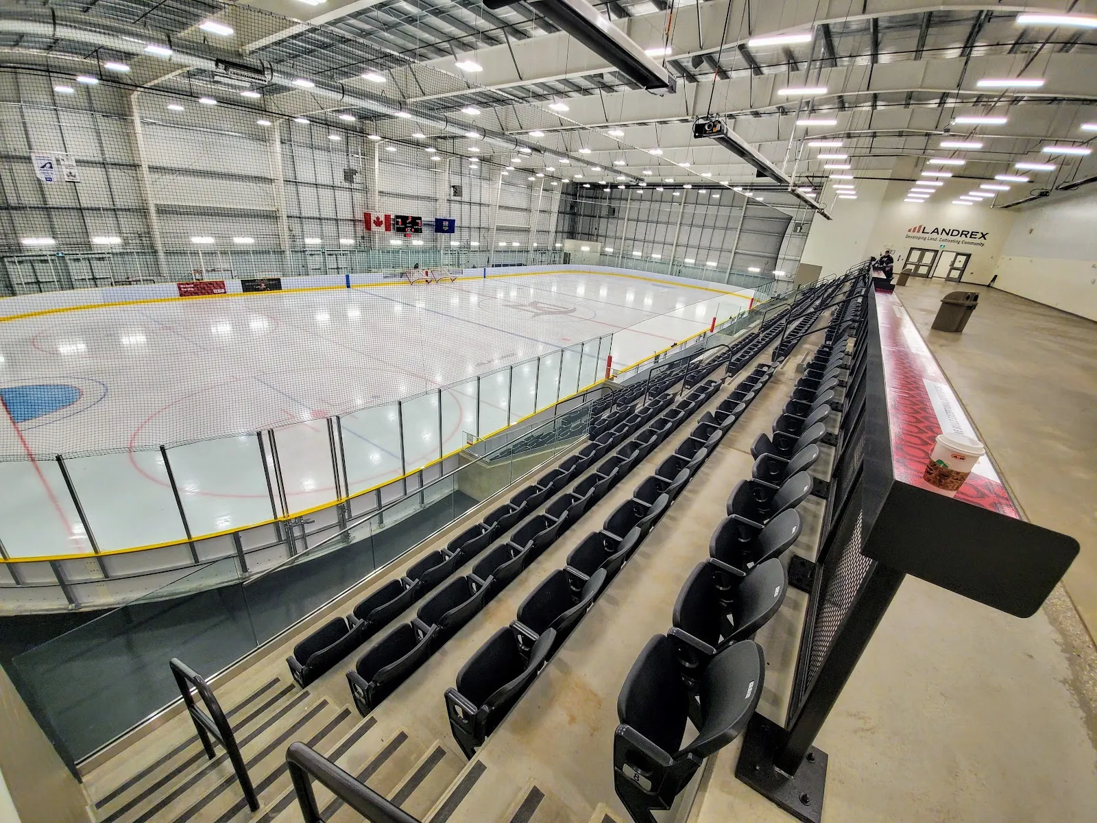 The empty ice sheet in the Morinville Leisure Centre arena with raked seating and a steel roof overhead. — Morinville Leisure Centre