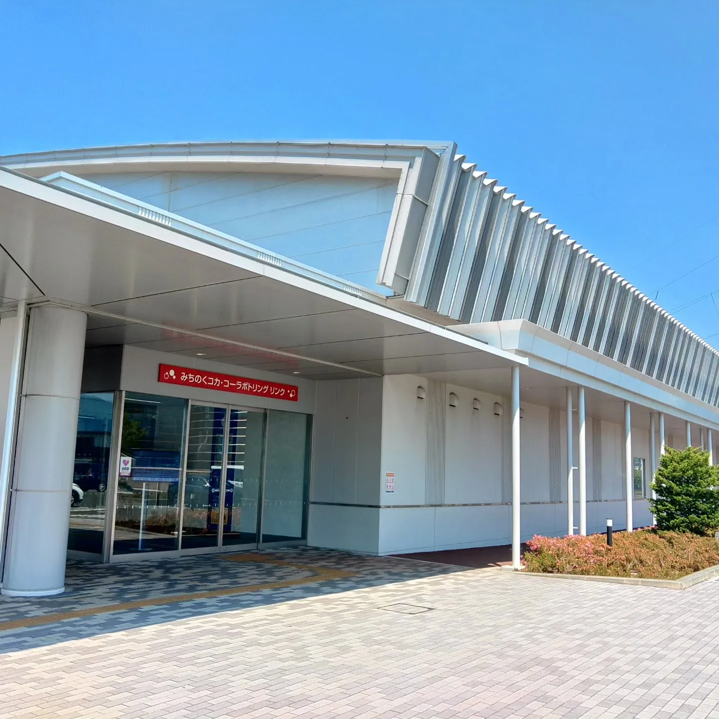 The canopied entrance of the Morioka City Ice Rink on a clear day, with the Michinoku Coca-Cola Bottling Rink sign above the glass doors. — Morioka City Ice Rink
