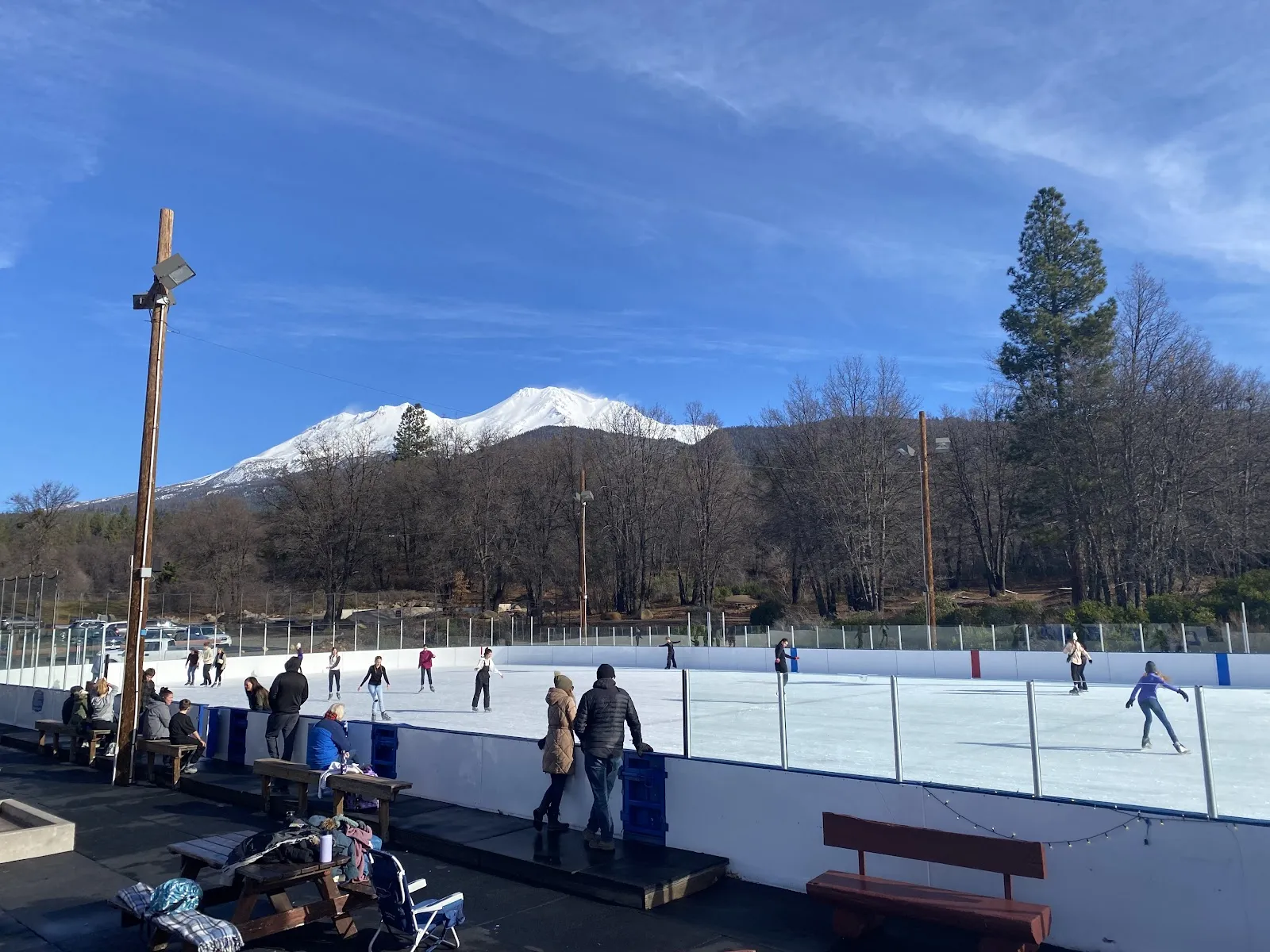 Skaters on the outdoor Mount Shasta Ice Rink on a sunny day with the snow-covered mountain behind — Mount Shasta Ice Rink