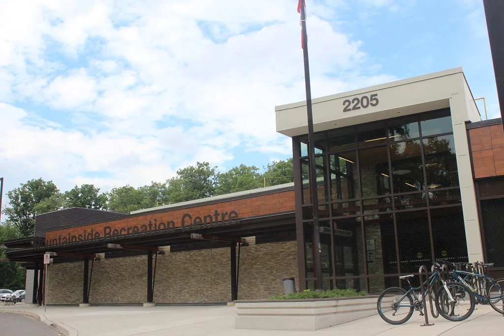 Front entrance of Mountainside Recreation Centre, glass entry under a wood-paneled canopy reading "Mountainside Recreation Centre", address number 2205 above the door, bike racks out front — Mountainside Arena (Mountainside Community Centre)