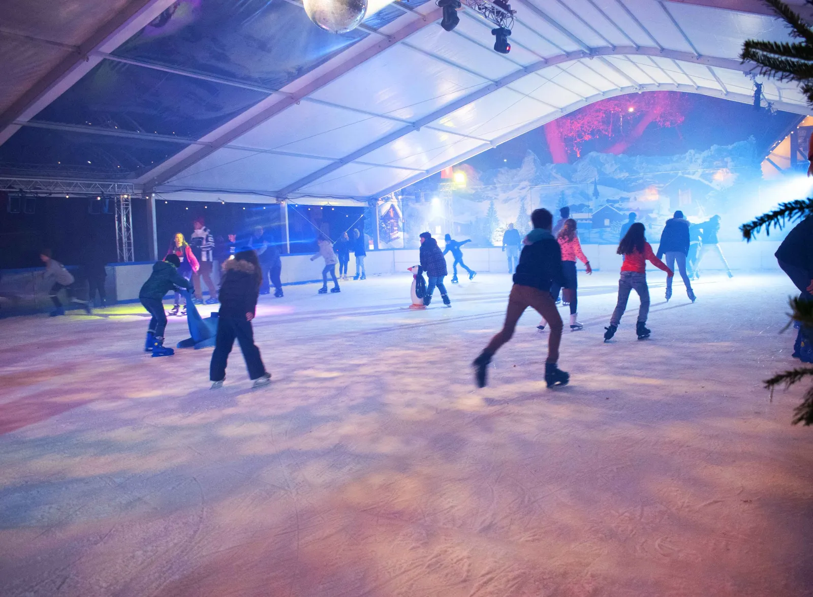 Die überdachte Pop-up-Eisbahn der Mr.F EISWELT in Neustadt an der Weinstraße unter ihrem weißen Zeltdach, mit Schlittschuhläufern auf dem Eis und blauem Abendlicht – Mr.F EISWELT Neustadt a.d.W.