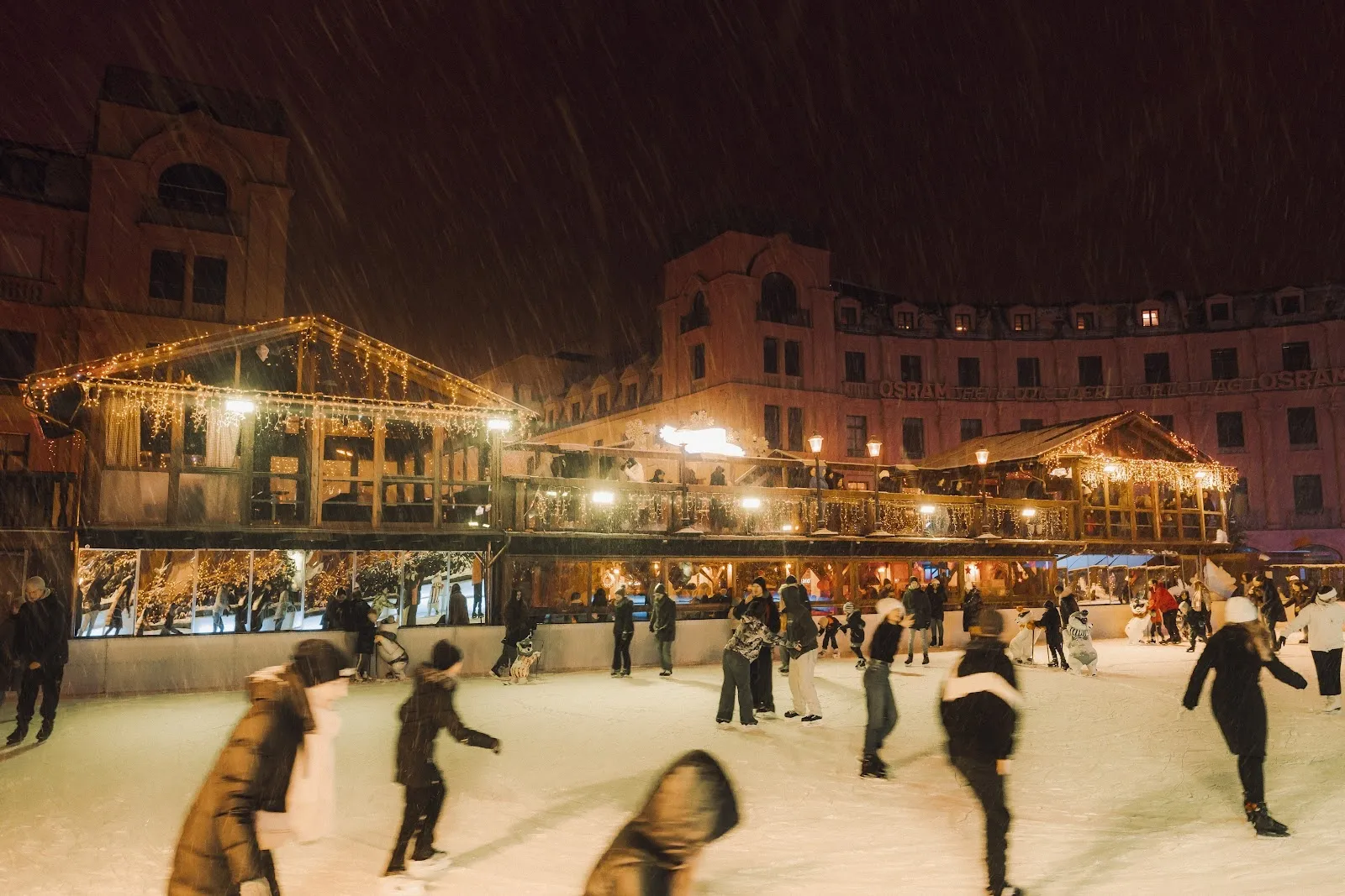 Die Eisbahn des Münchner Eiszaubers am Stachus bei Nacht, mit Schlittschuhläufern auf dem Eis und den beleuchteten Holzhütten rund um die Fläche. – Münchner Eiszauber am Stachus